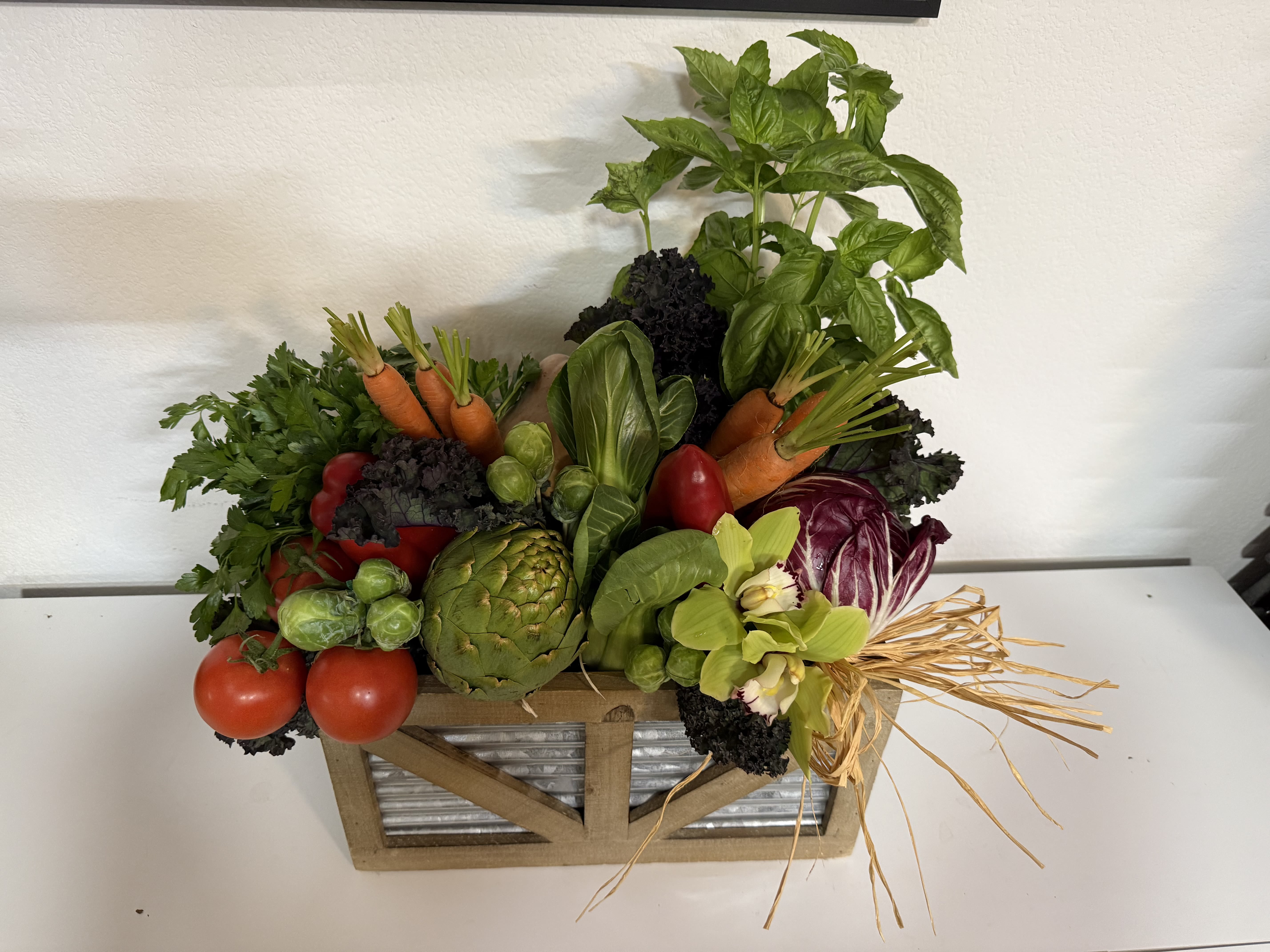 Vegetable arrangement in a wooden crate with basil, carrots, tomatoes, artichoke, and cabbage
