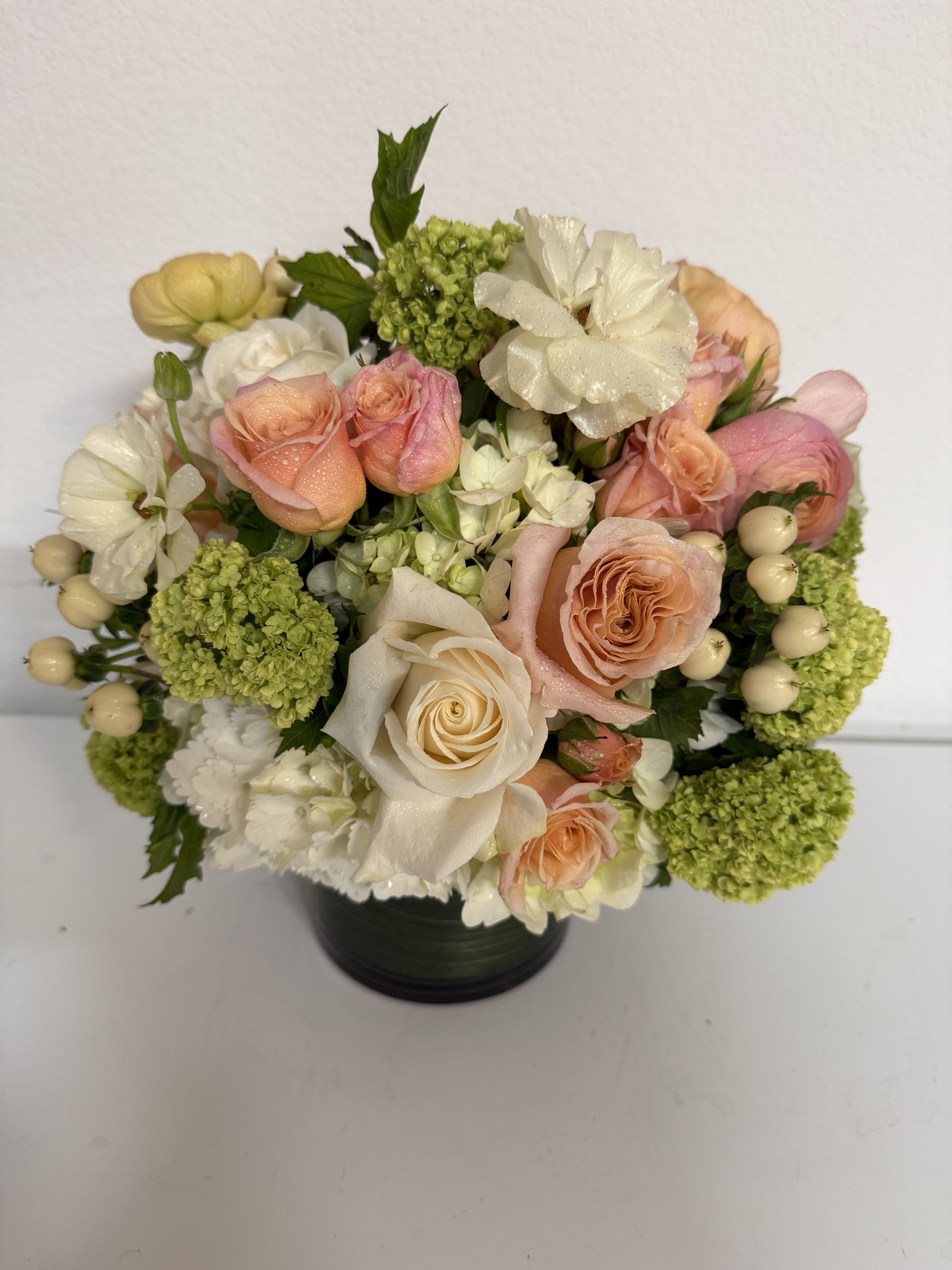 Bouquet of peach and white roses with green hydrangeas in a black vase