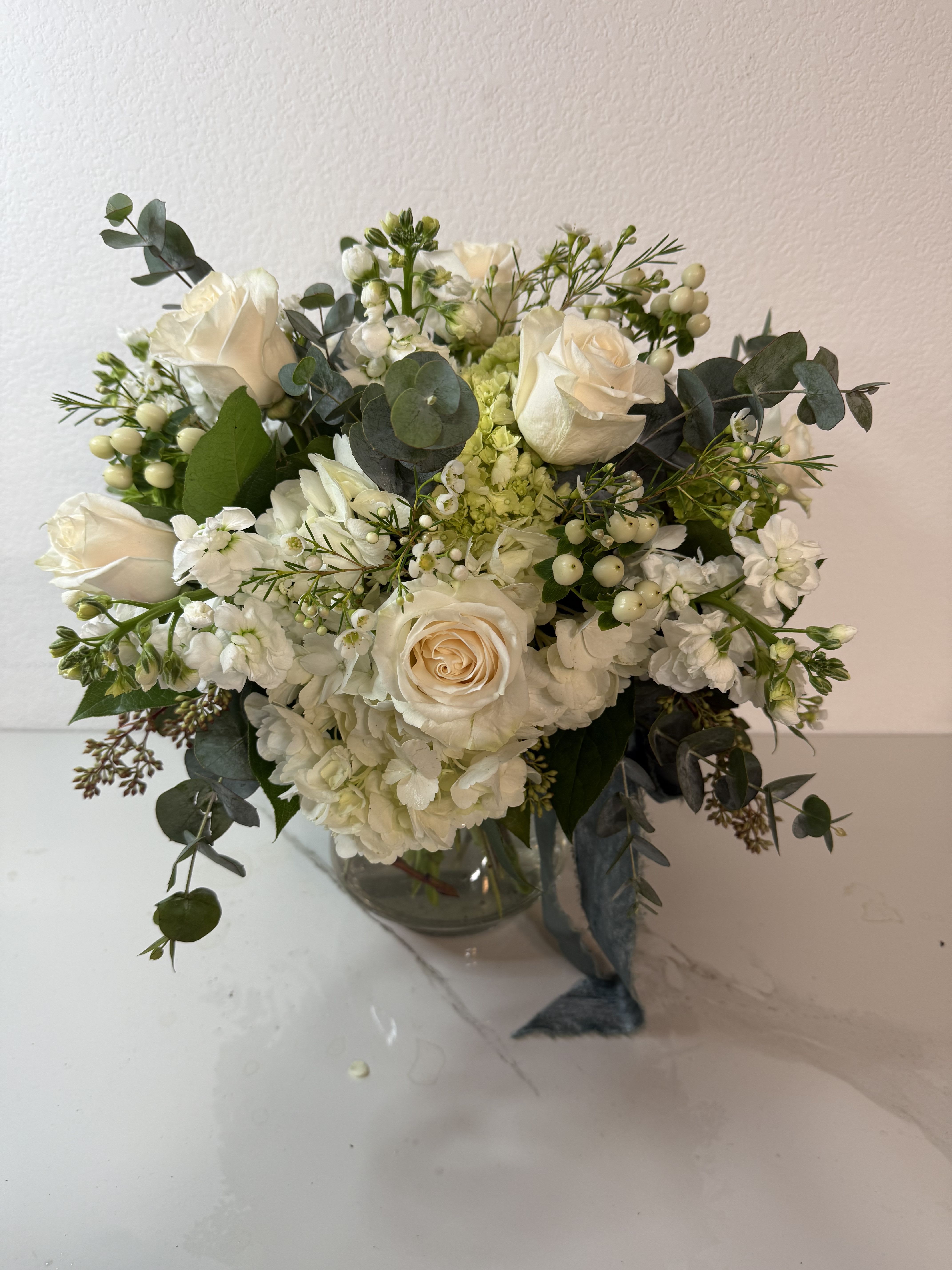 White rose bouquet in a clear glass vase with eucalyptus and small white filler flowers