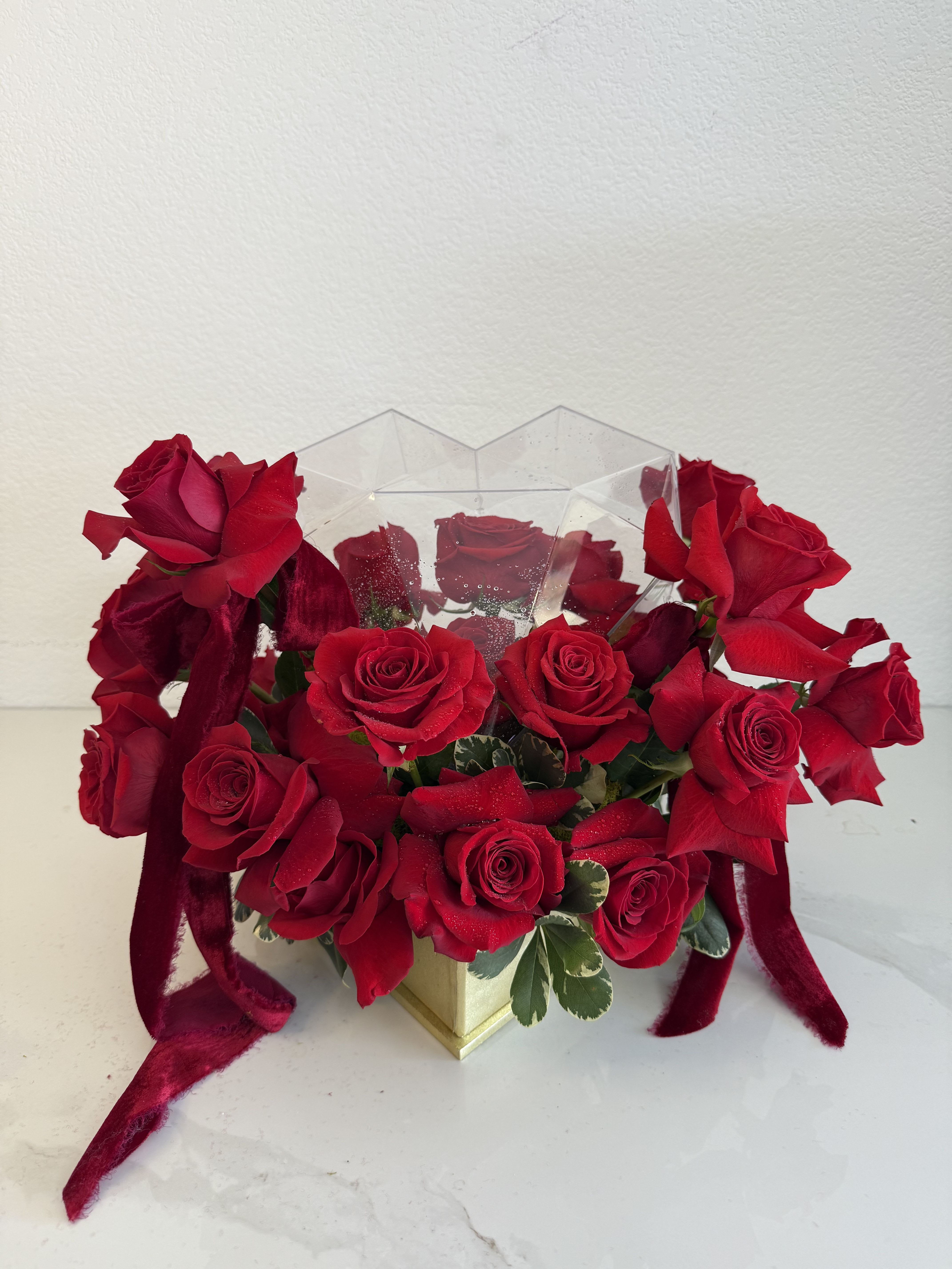 Red roses arranged in a clear geometric box with ribbon accents