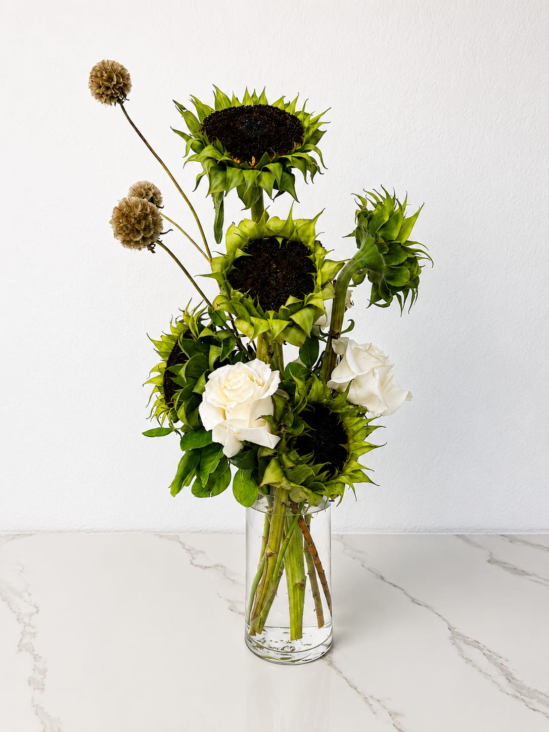 Tall arrangement of green sunflowers and white roses in a clear glass vase