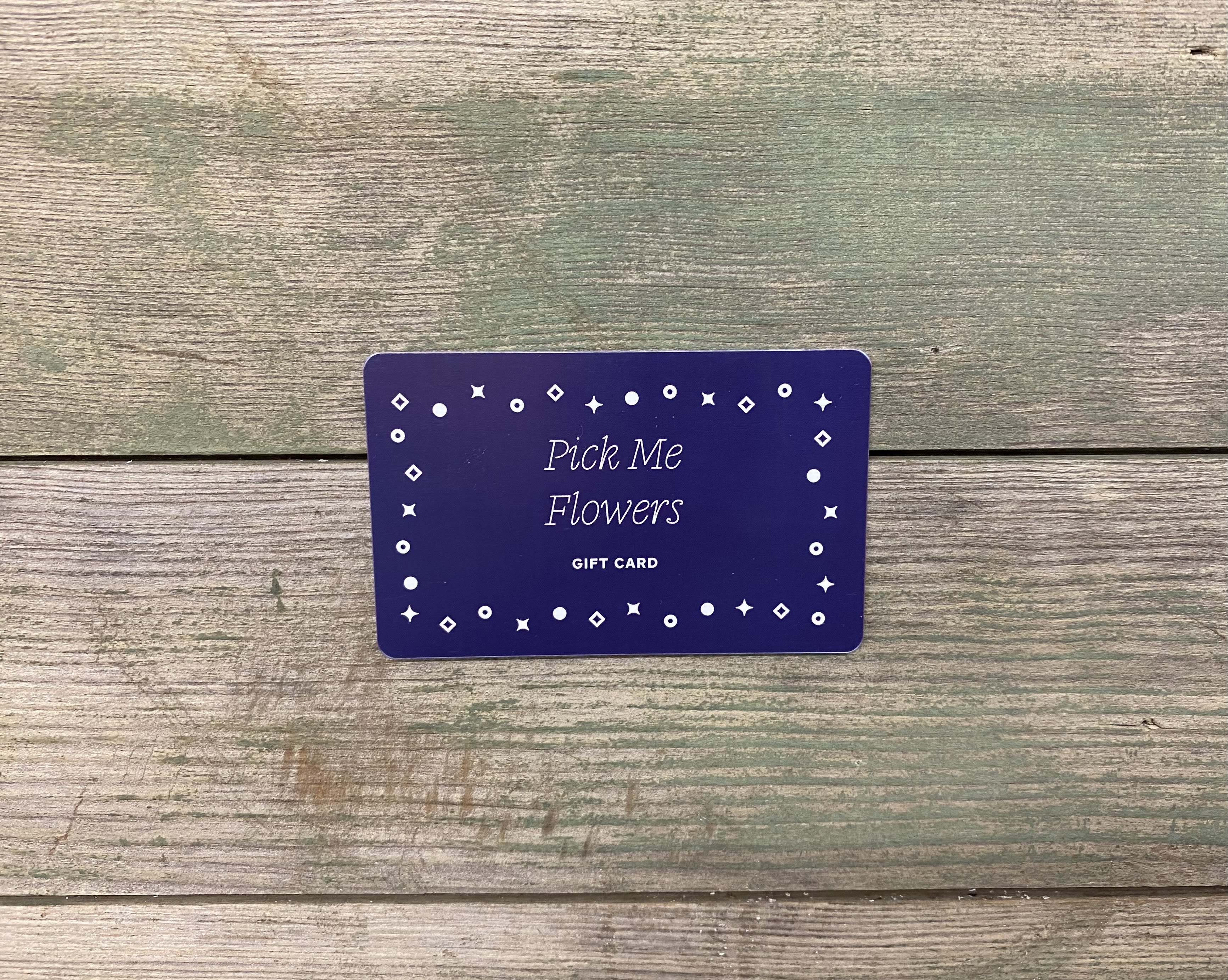 Purple Pick Me Flowers gift card on a wood surface