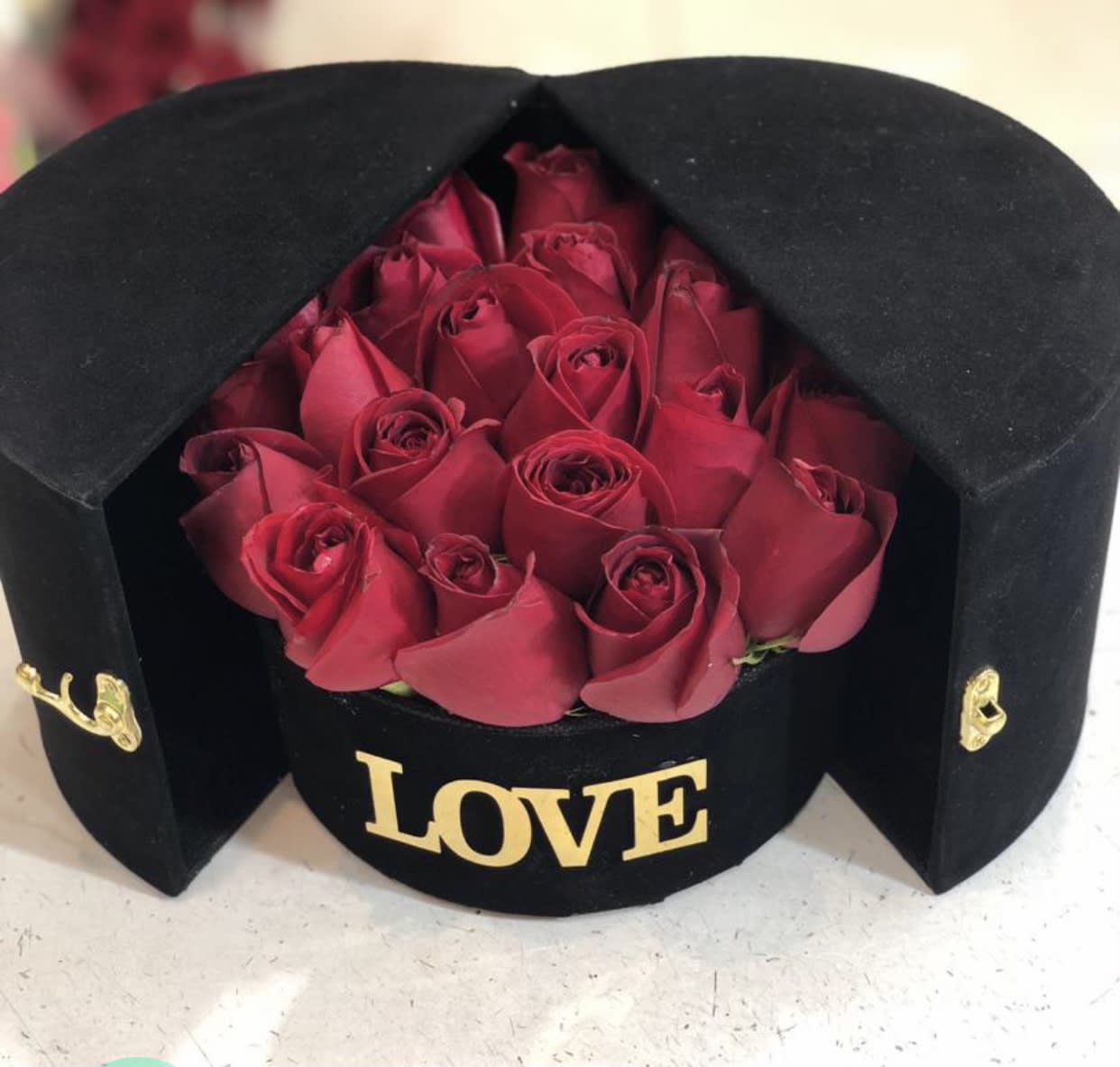 Red roses in a black hatbox with gold "LOVE" lettering
