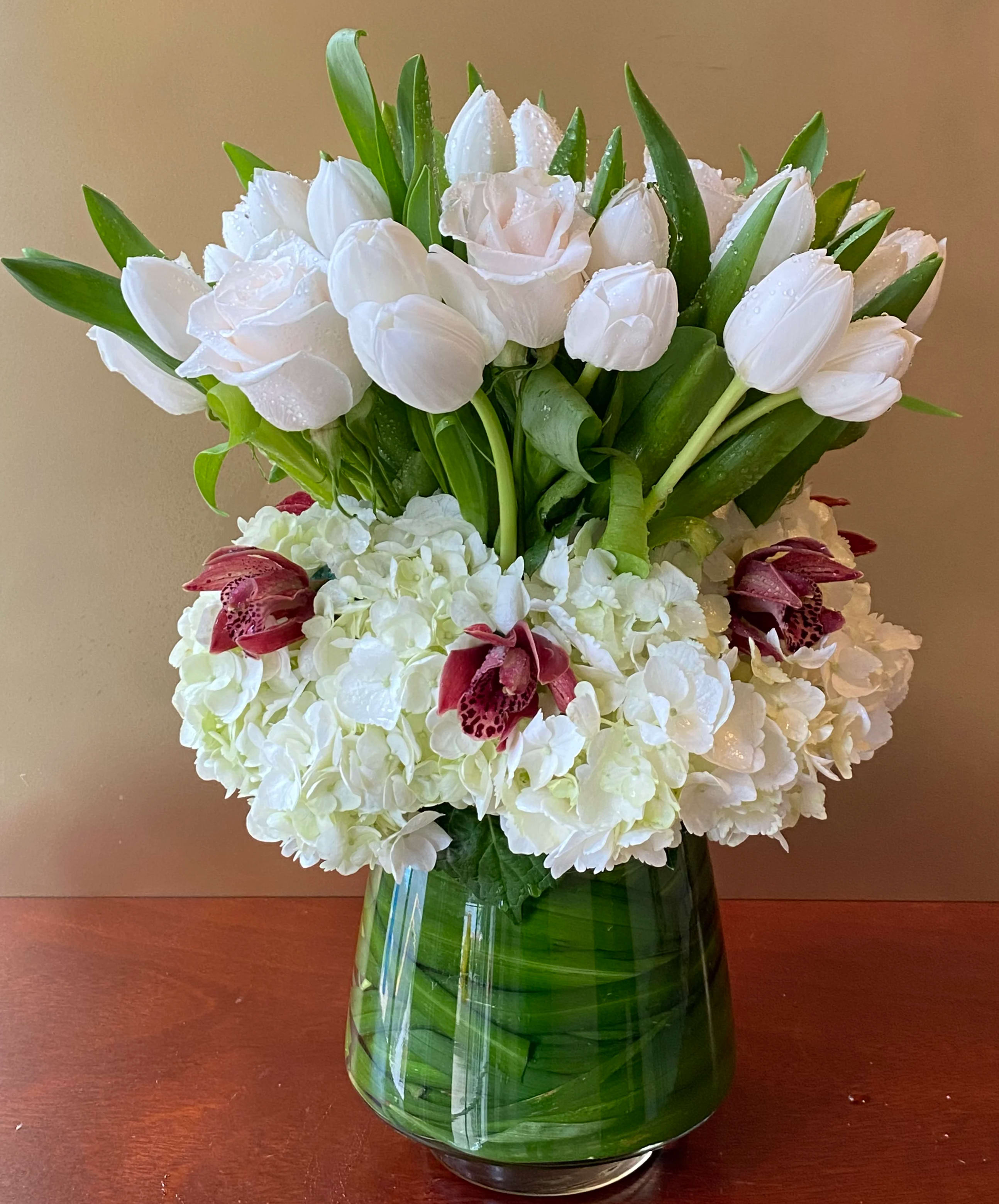 White tulips and hydrangeas with burgundy orchids in a green glass vase