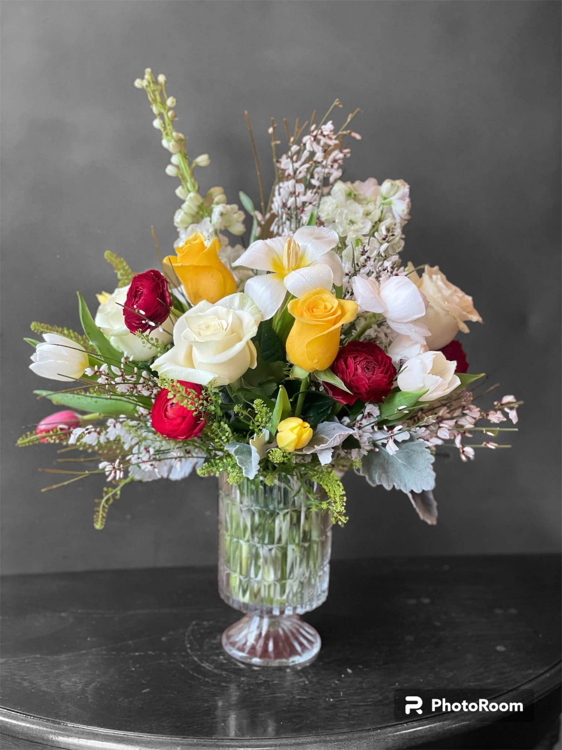 Mixed bouquet of roses, tulips, and white blooms in a clear glass vase