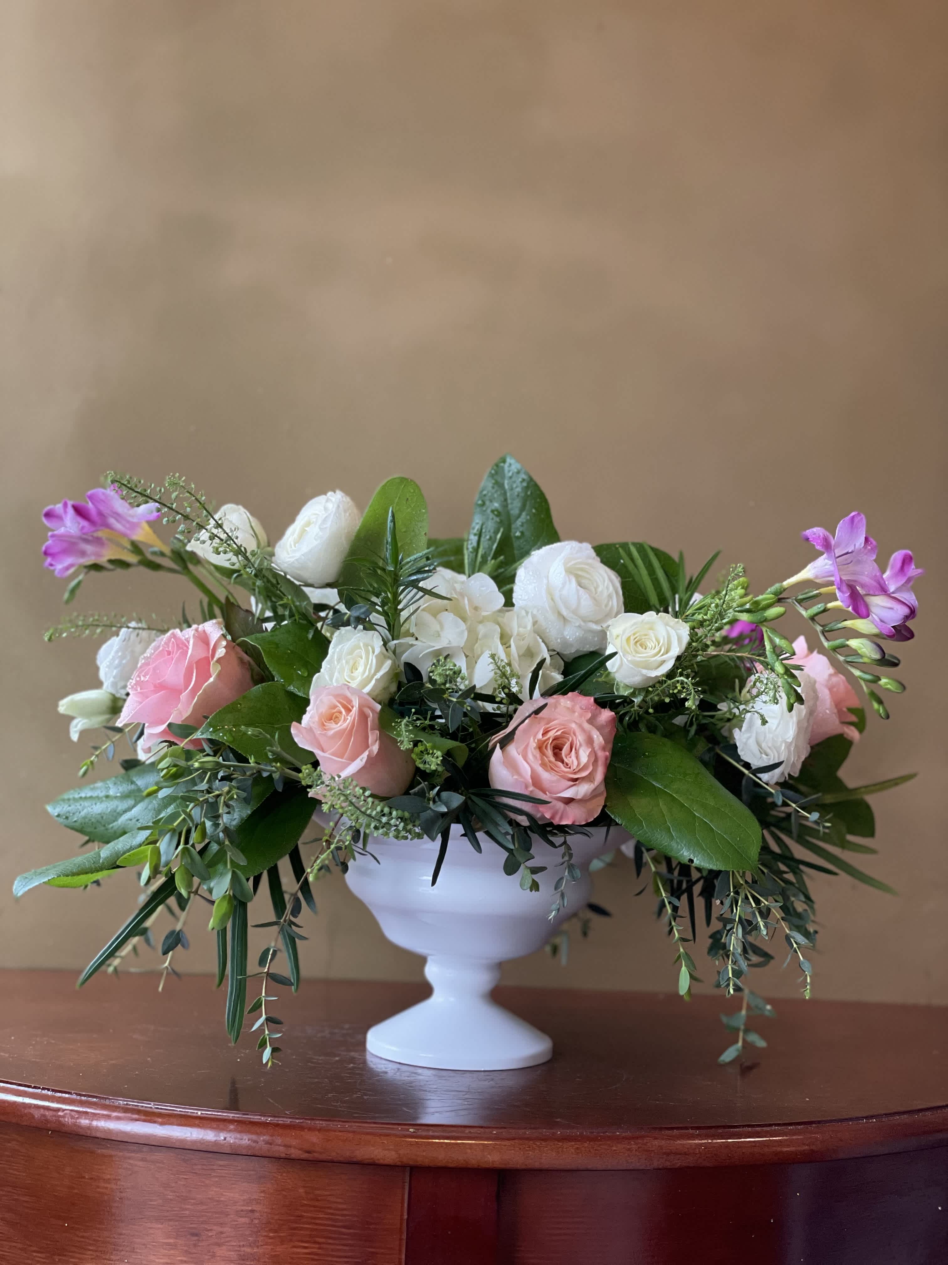 Pink and white roses arranged in a white pedestal vase