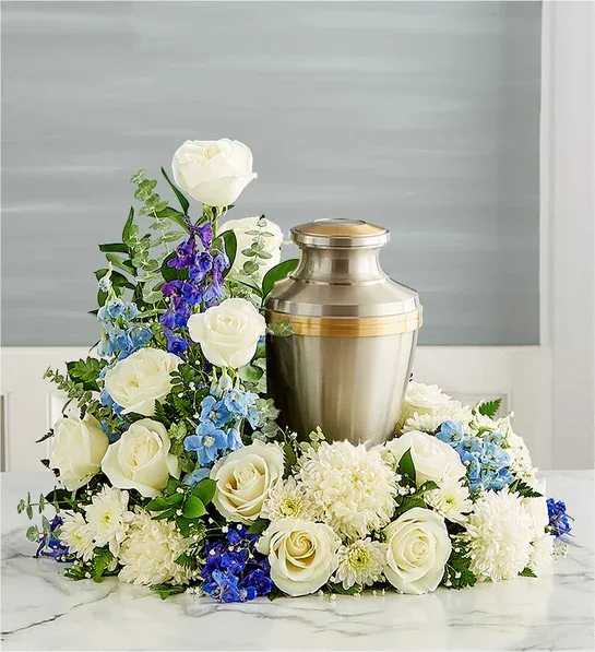 White roses and blue flowers arranged around a metal urn