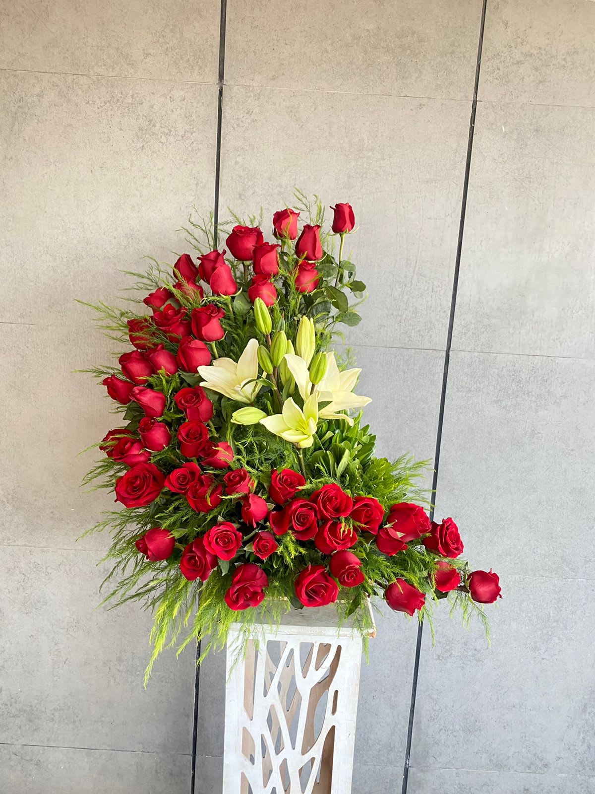 Large red rose and white lily arrangement in a white pedestal vase