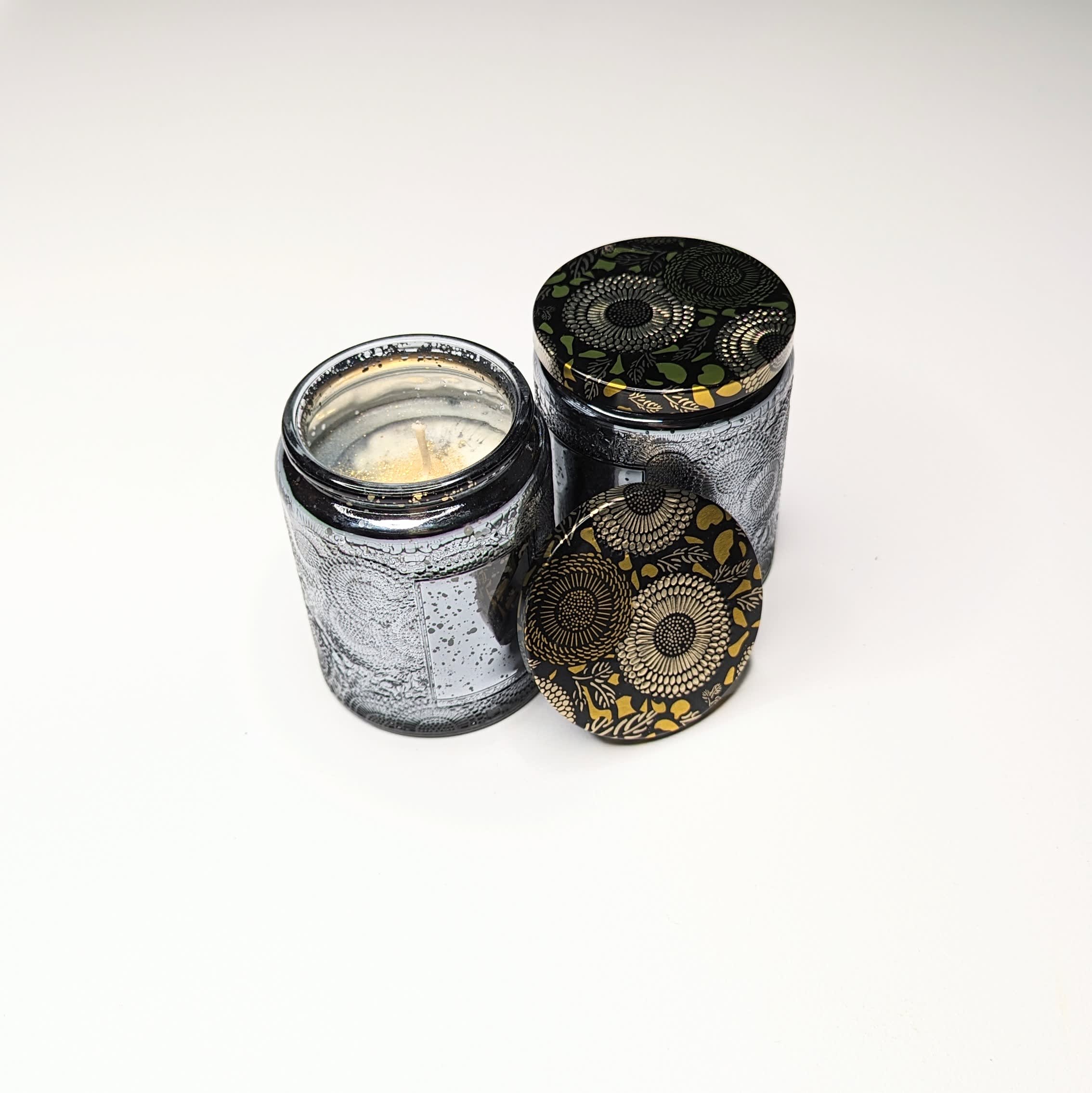 Two decorative candles in patterned glass jars with lids