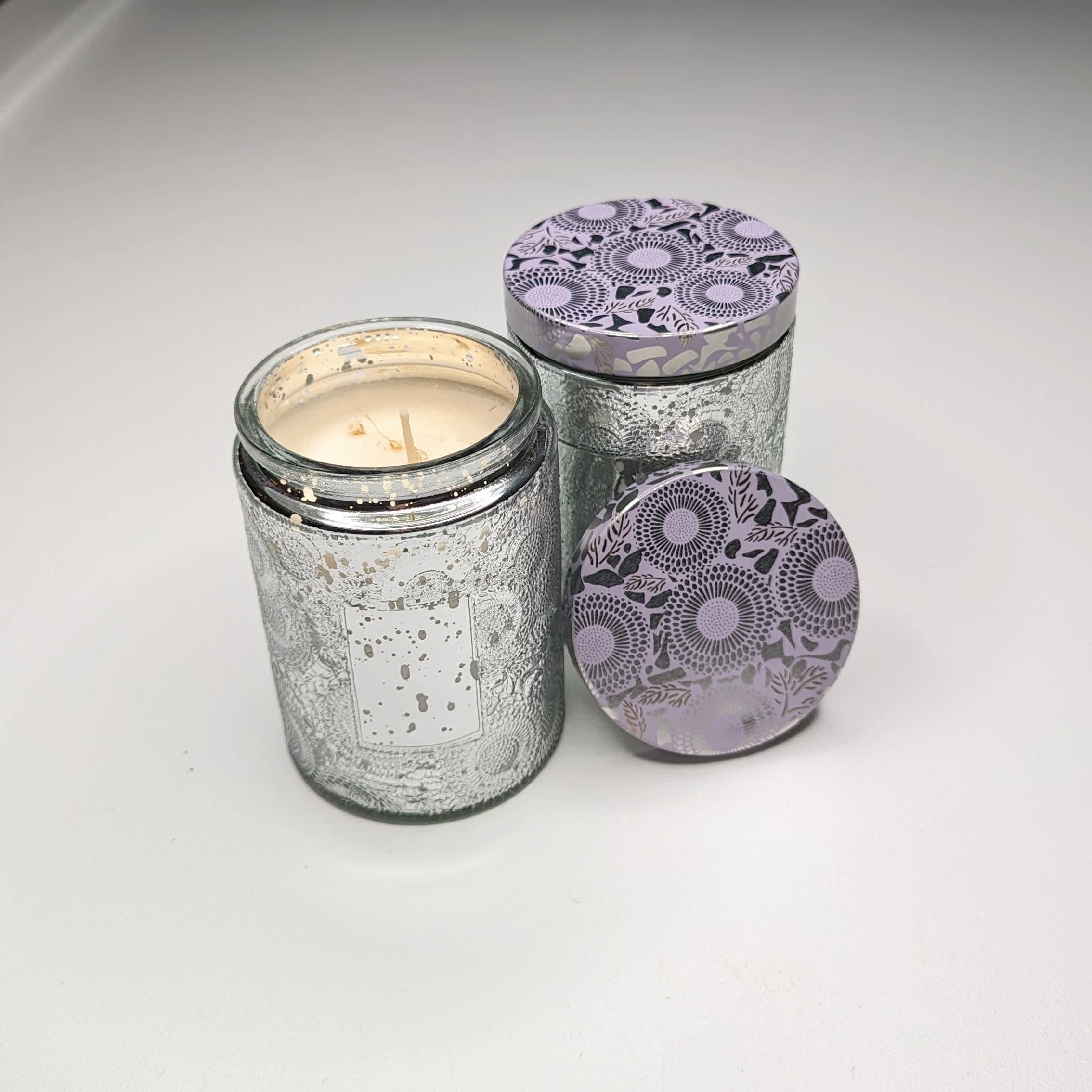Two glass jar candles with patterned lids on a white surface