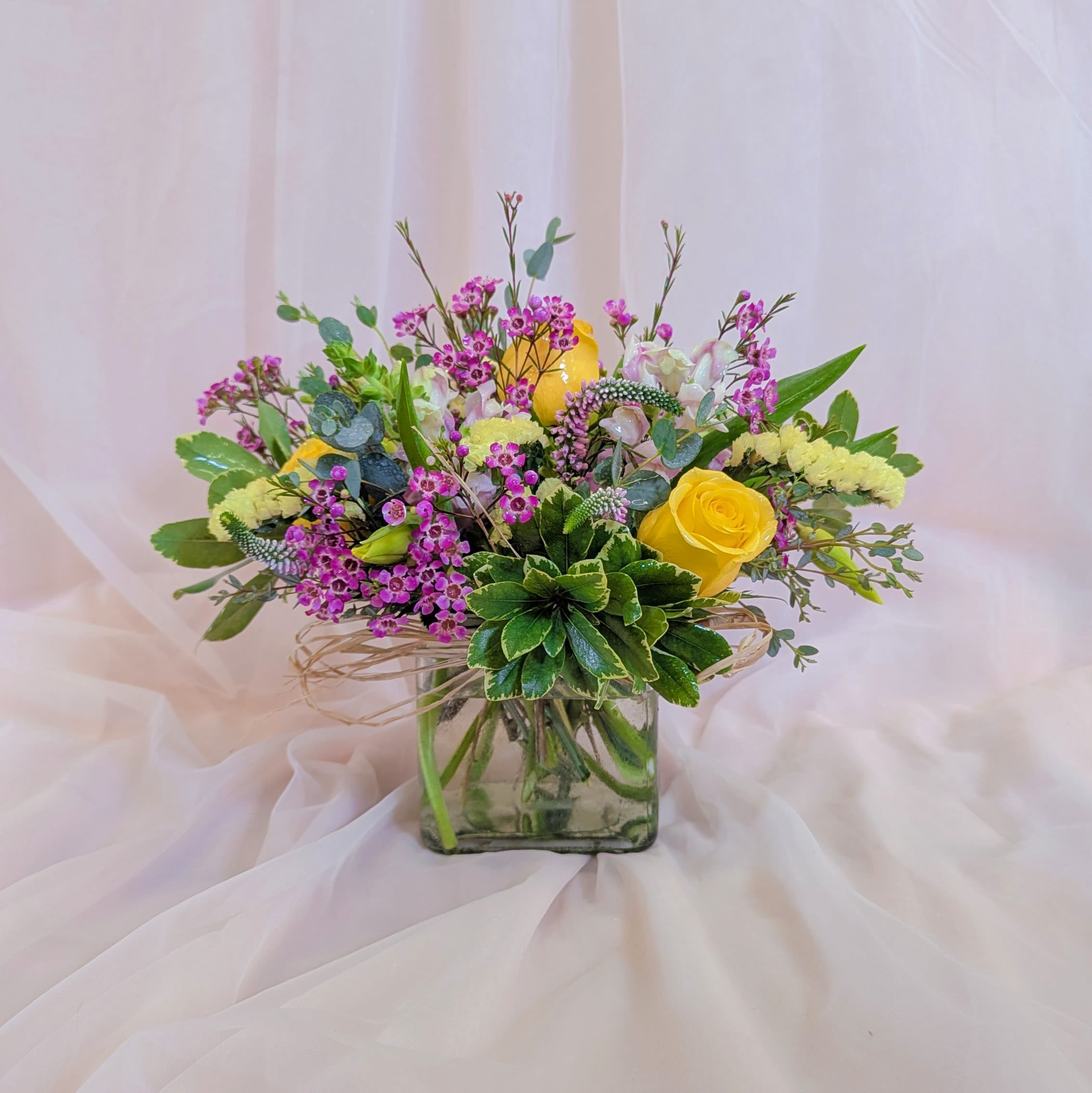 Bouquet of yellow roses and pink filler flowers in a square glass vase