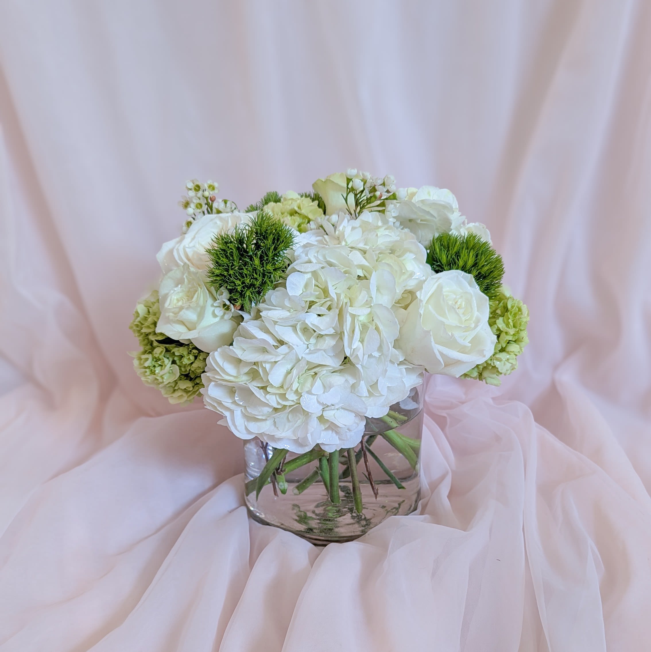 White floral bouquet in a clear glass vase with pale pink draping