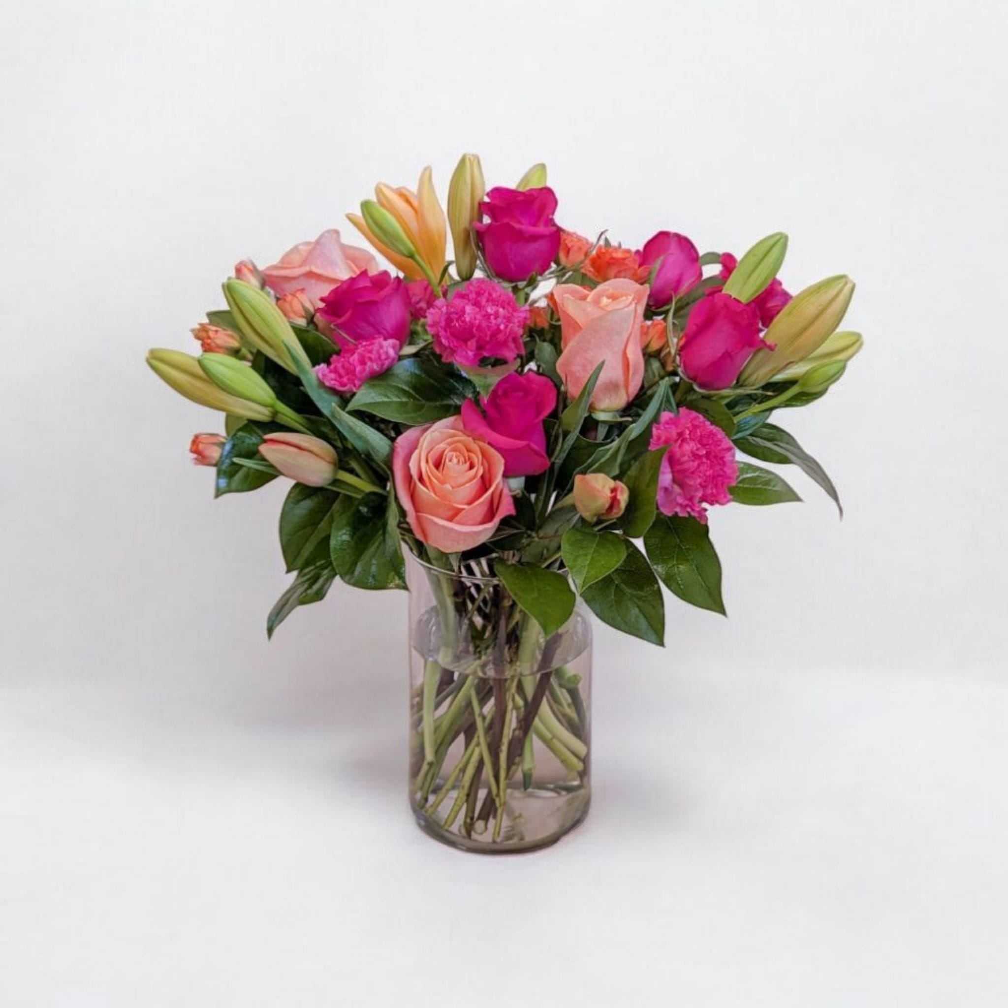 Pink and peach roses with lilies and carnations in a glass vase