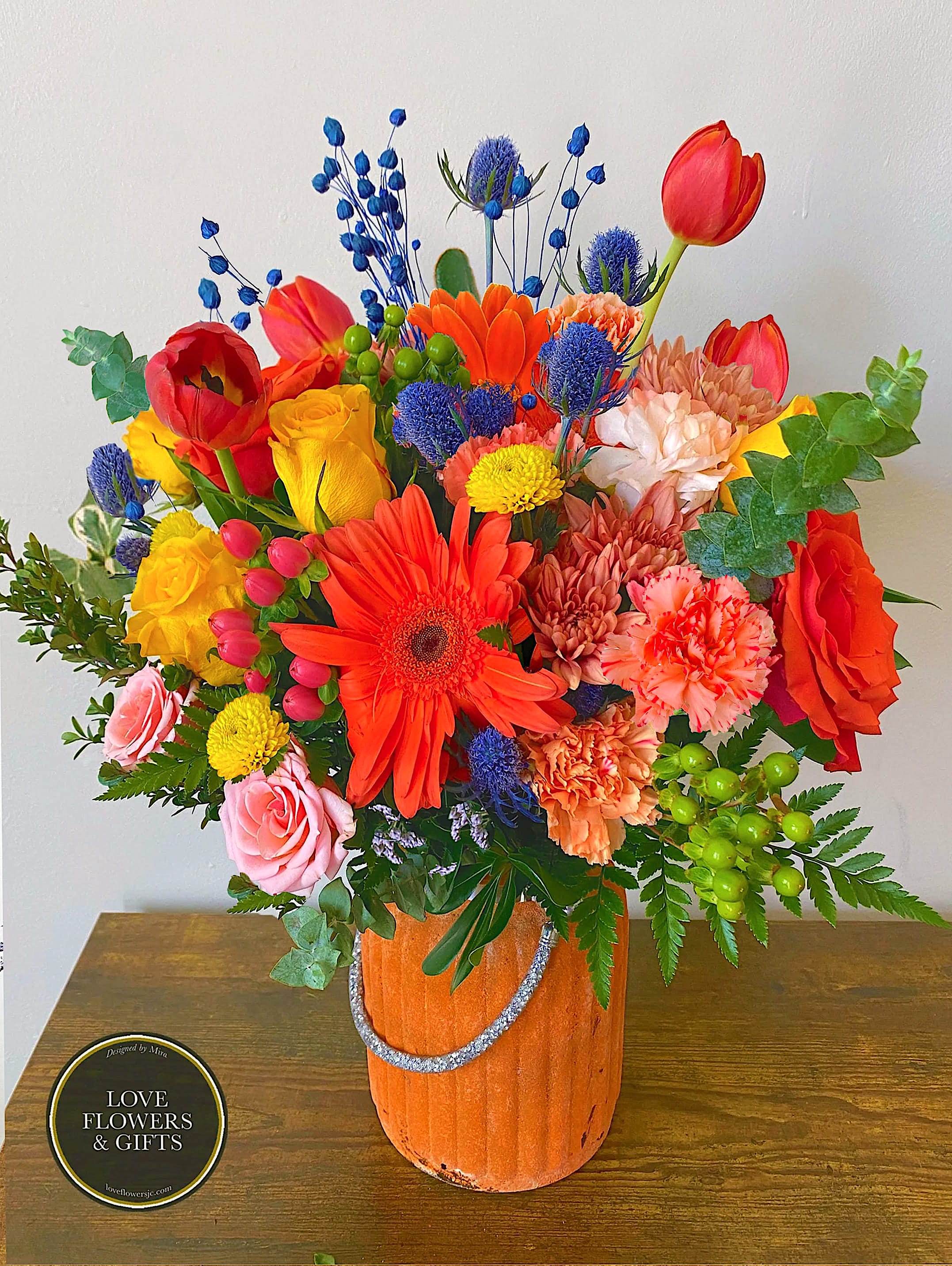 Bright mixed bouquet of orange, yellow, red, and pink flowers in an orange pot