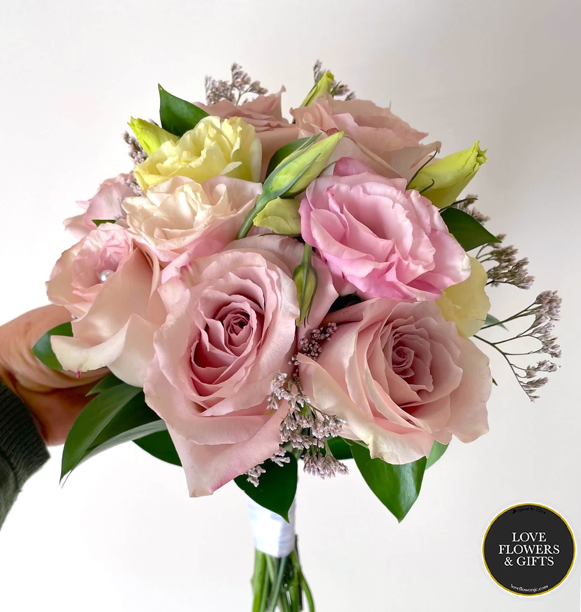 Hand-tied bouquet of pale pink roses and cream blooms held against a light background