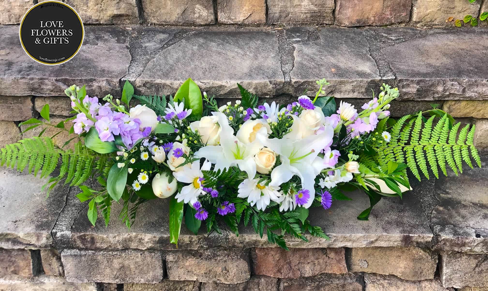 Low white lily and rose arrangement with purple and white daisies and ferns on stone steps