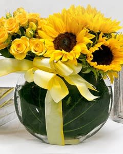 Yellow sunflowers and roses in a round glass vase with a yellow ribbon