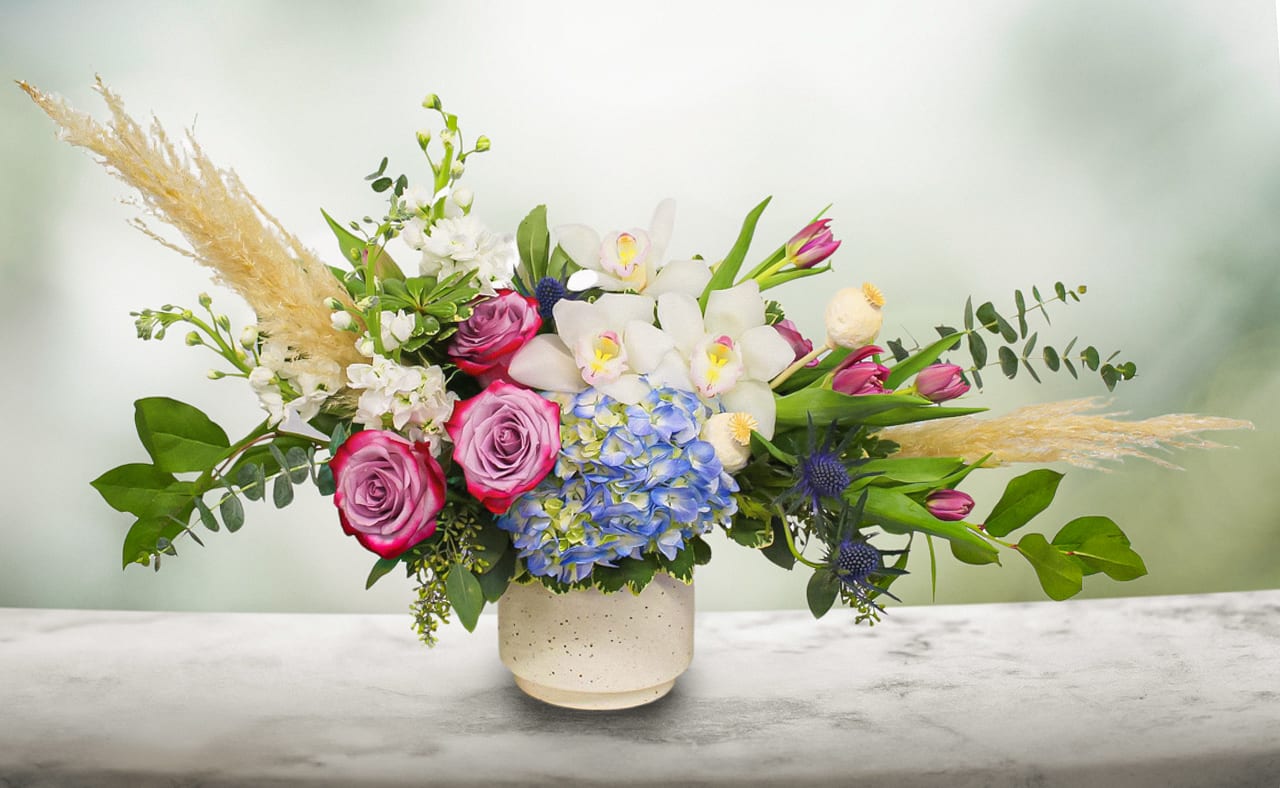 Mixed bouquet with pink roses, white orchids, and blue hydrangea in a ceramic vase