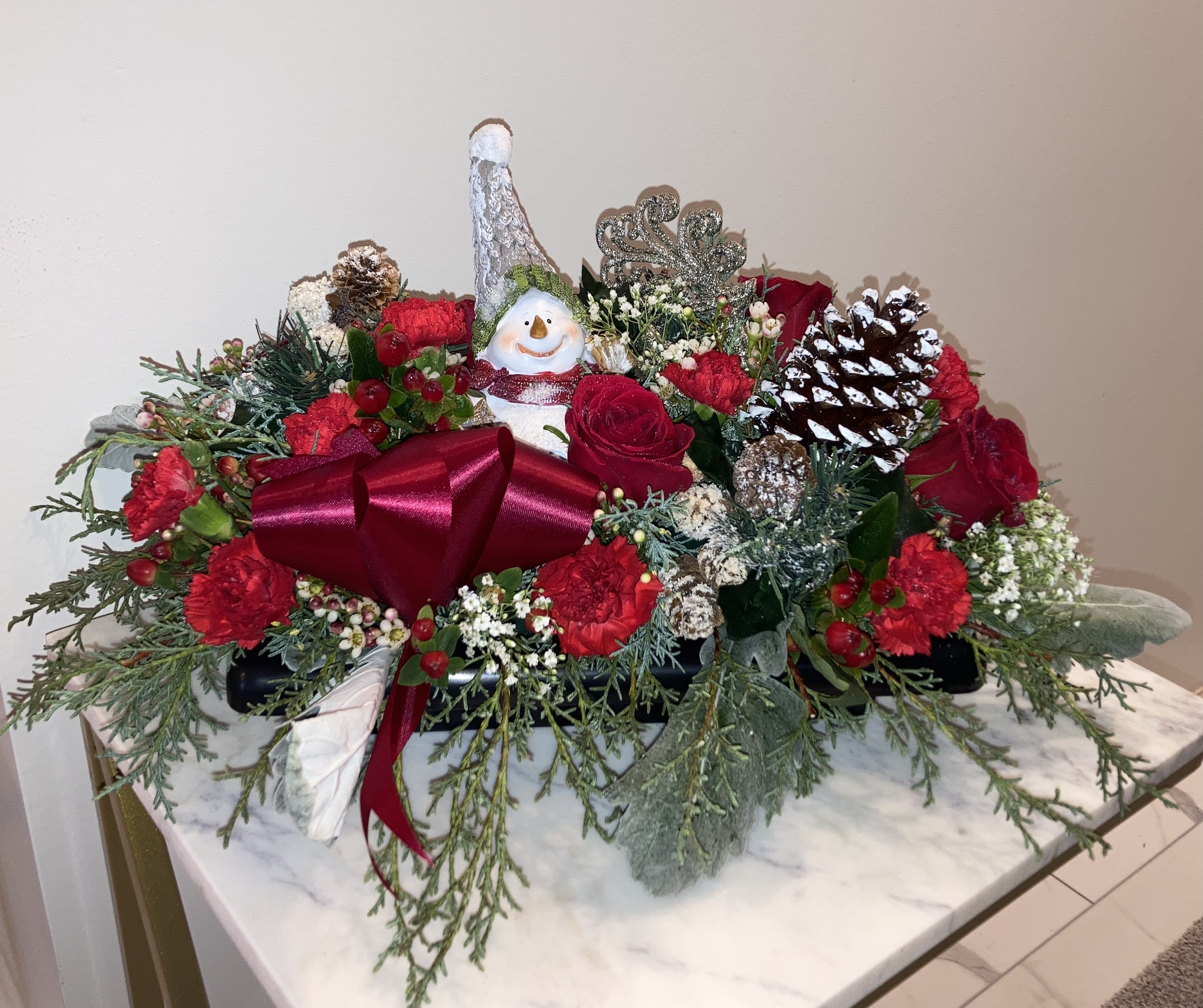 Christmas floral centerpiece with red flowers, pinecones, and a snowman ornament