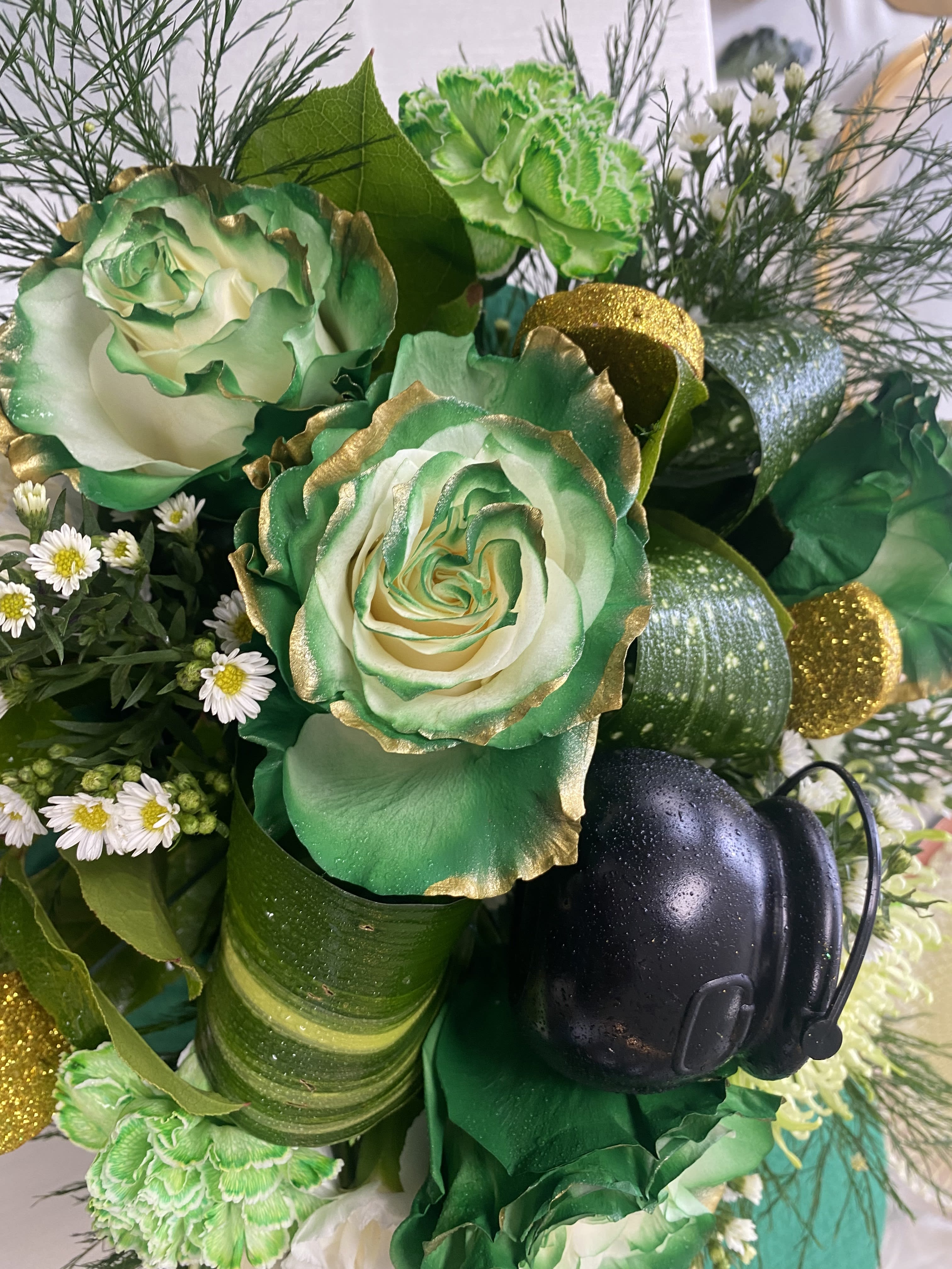 Green and white floral arrangement with gold accents and a black firefighter helmet