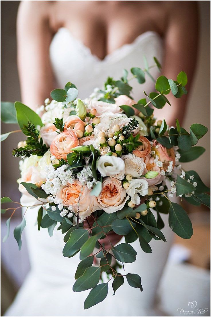 Bride holding a bouquet of peach and white flowers with greenery