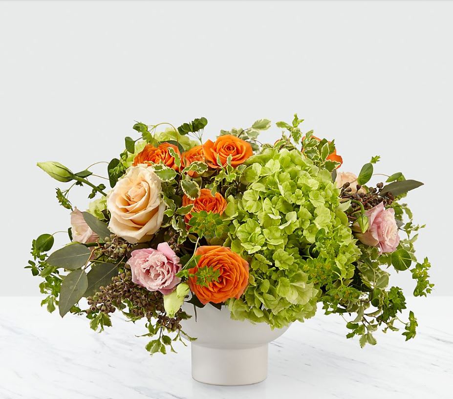 Orange and blush roses with green hydrangea in a white vase