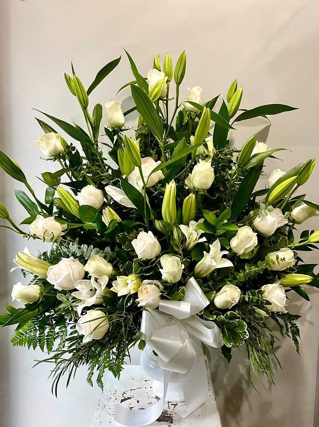 Large white lily and rose arrangement in a white vase with ribbon