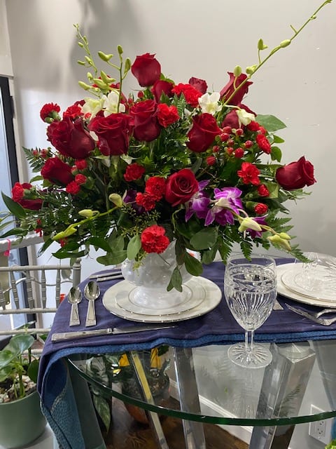 Red rose centerpiece in a clear glass vase on a set table