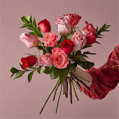 Hand-tied bouquet of red and pink roses held against a pink background