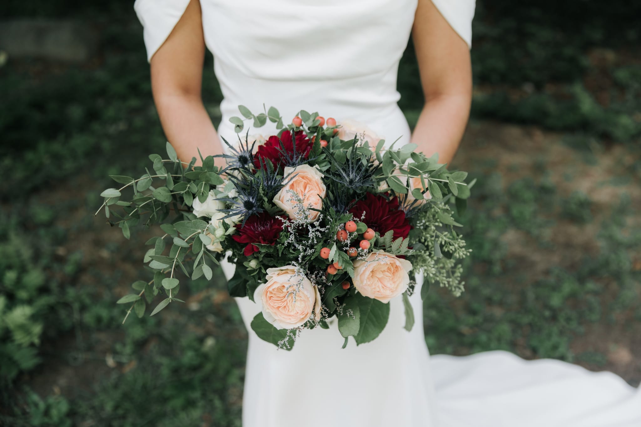 Bride holding a bouquet of peach and burgundy flowers with greenery