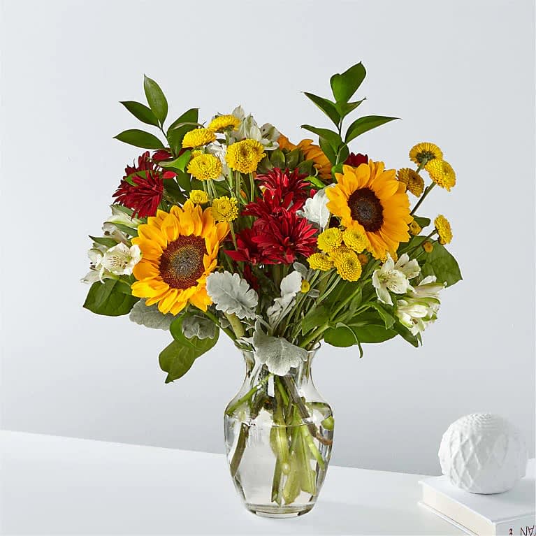 Bouquet of sunflowers, red blooms, and white flowers in a glass vase