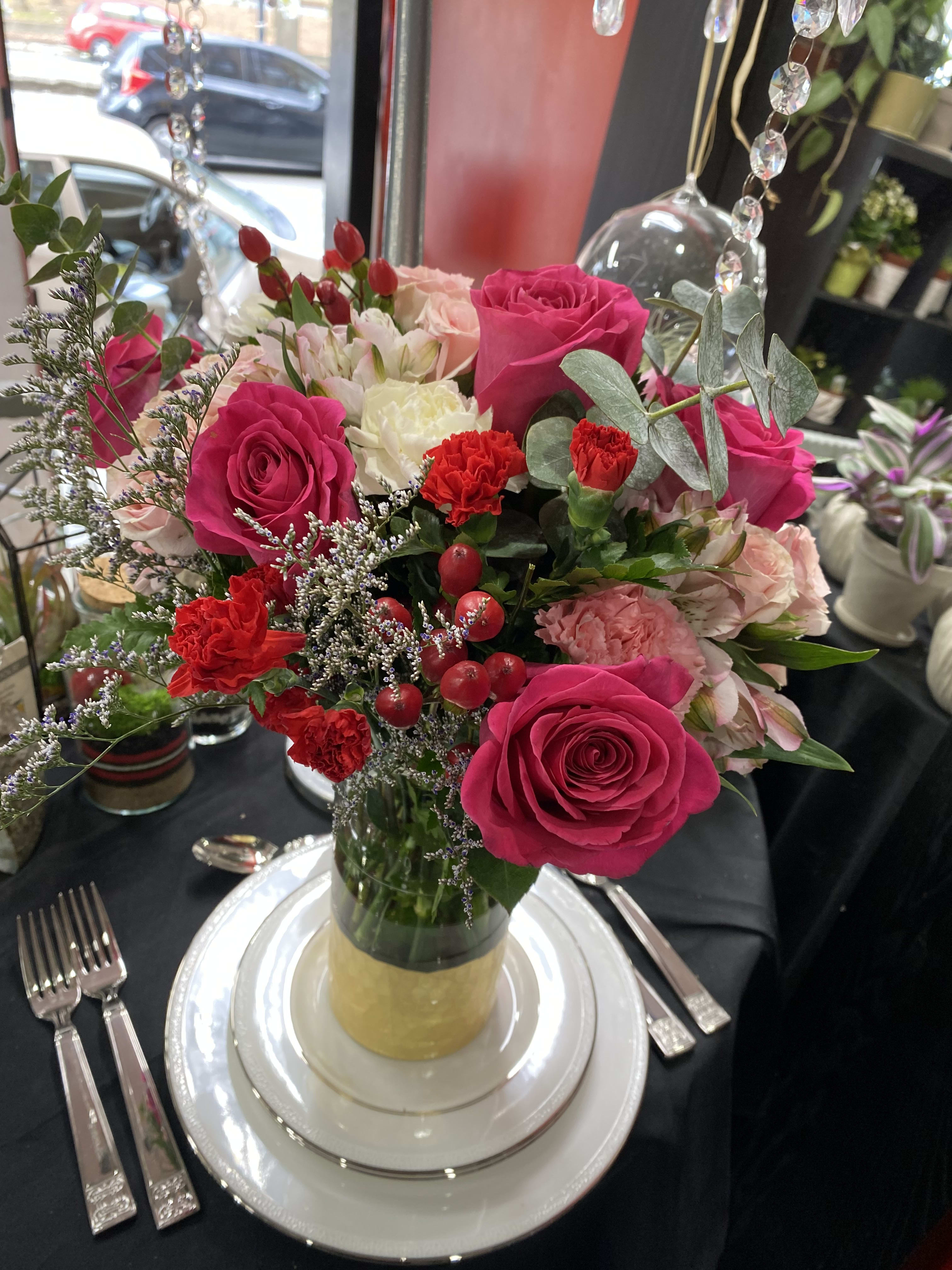 Pink and red rose centerpiece in a glass vase on a set table