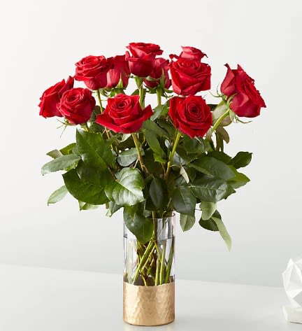 Red roses arranged in a clear glass vase with a gold base