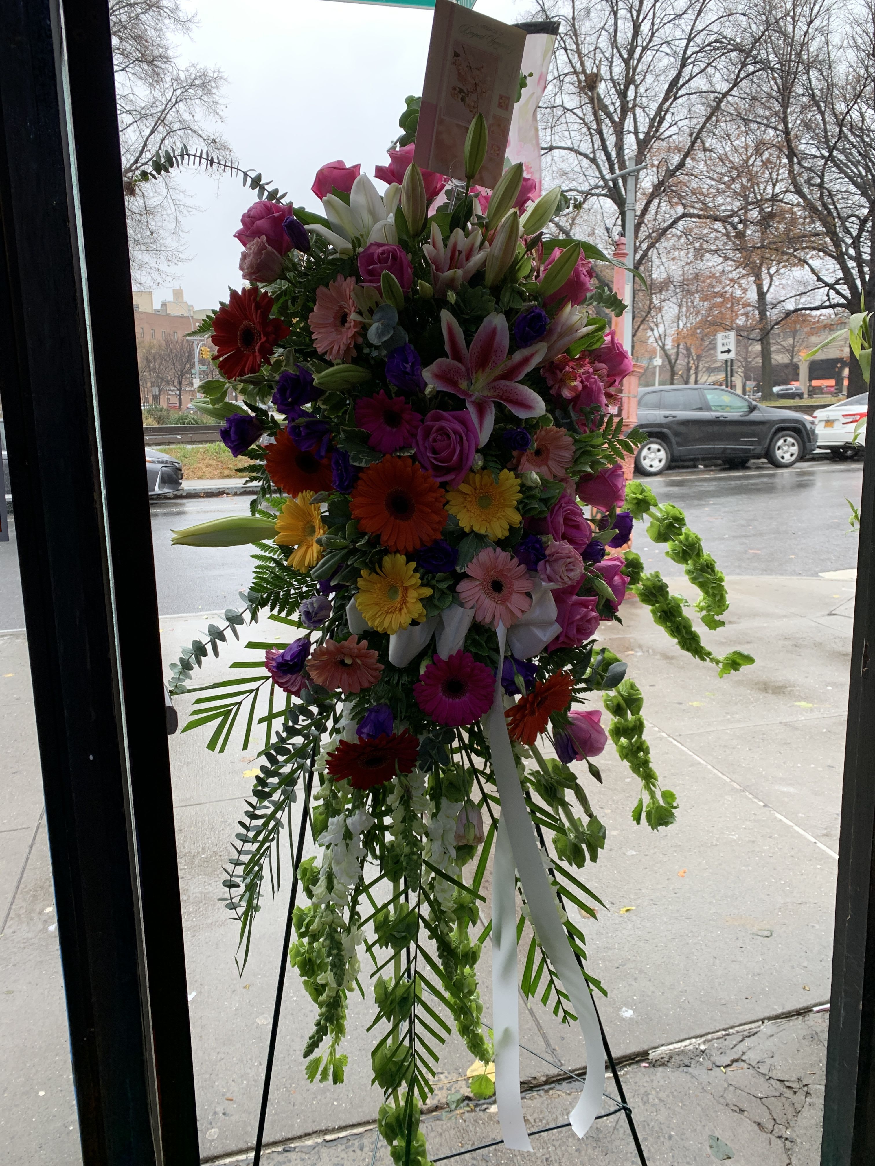 Tall standing spray of mixed pink, white, purple, and yellow flowers with ribbon