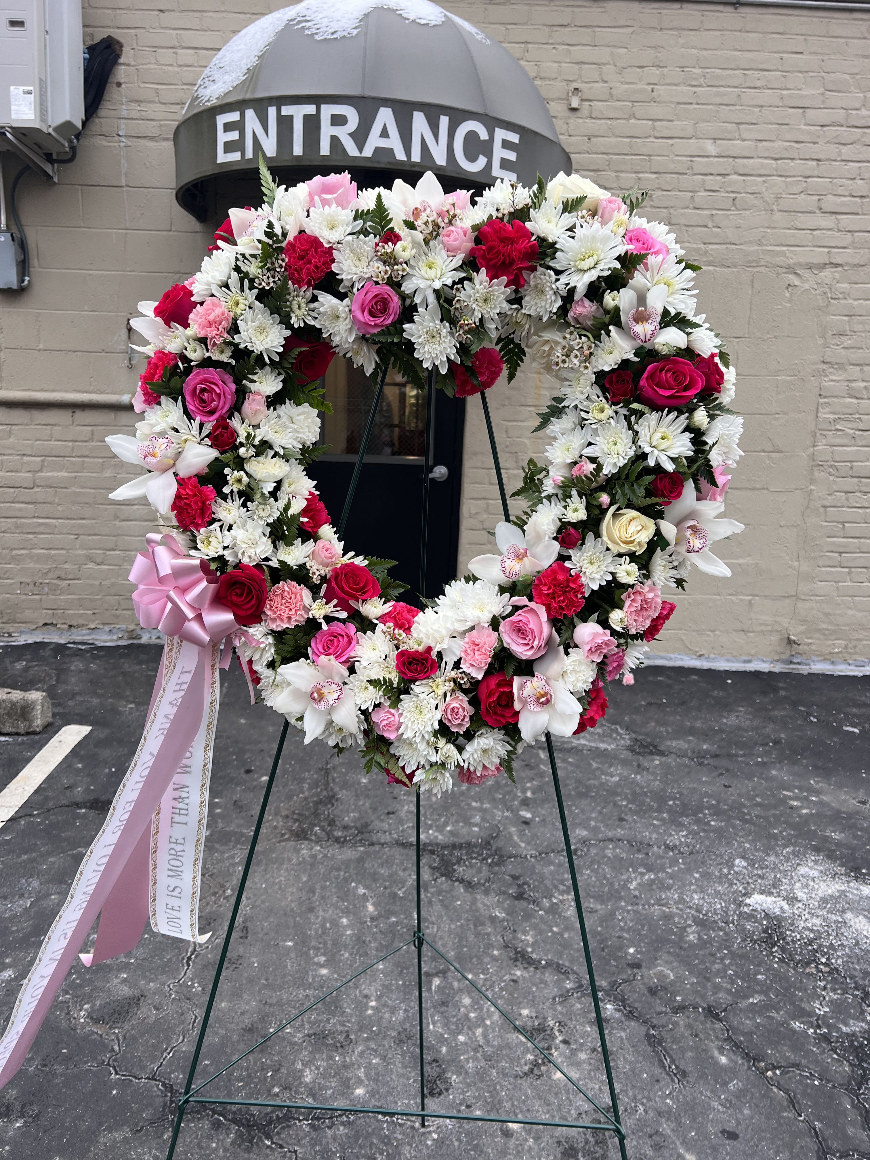 Heart-shaped floral wreath with pink, red, and white flowers on a stand