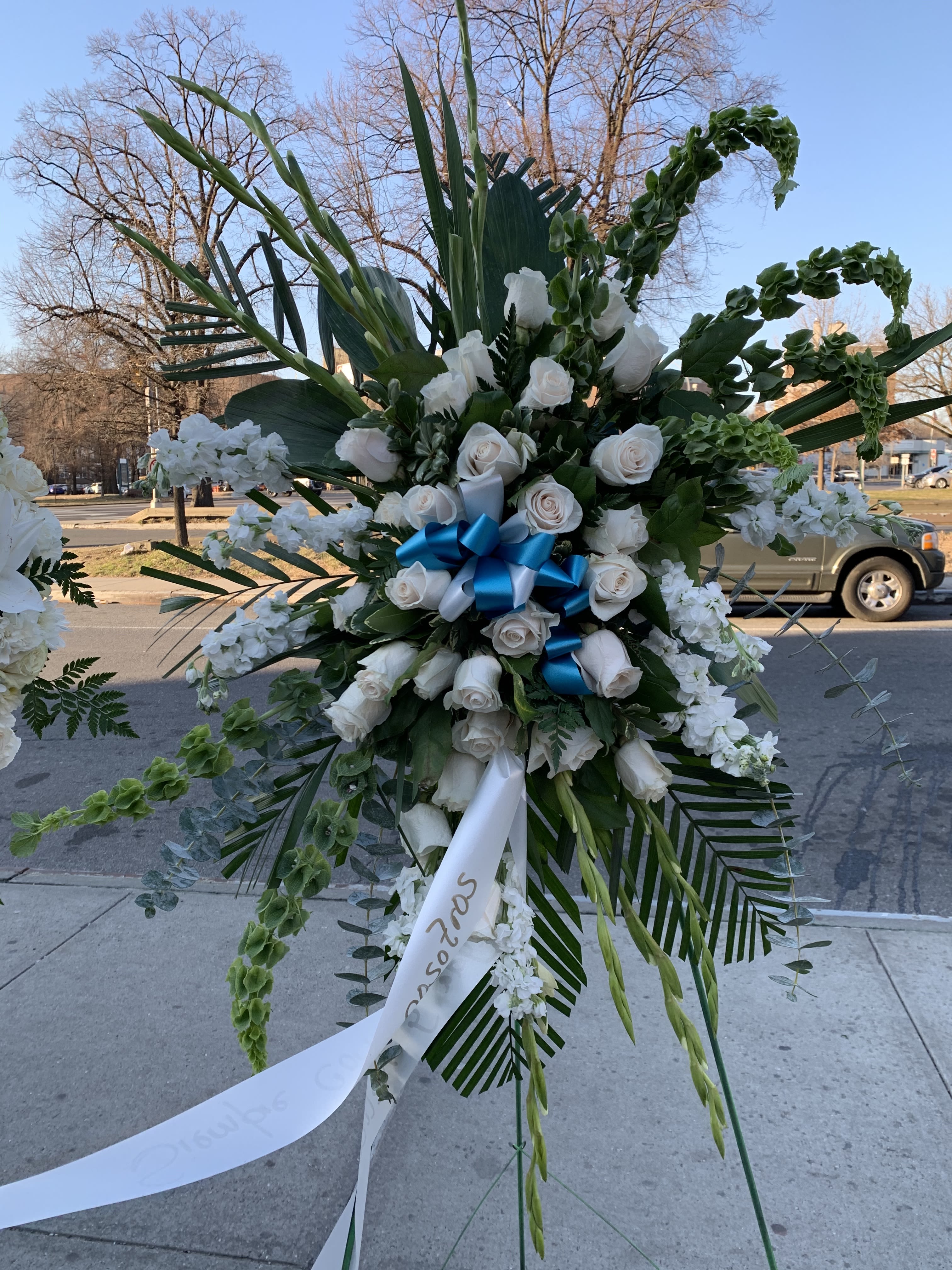 Large white rose standing spray with blue ribbon and greenery