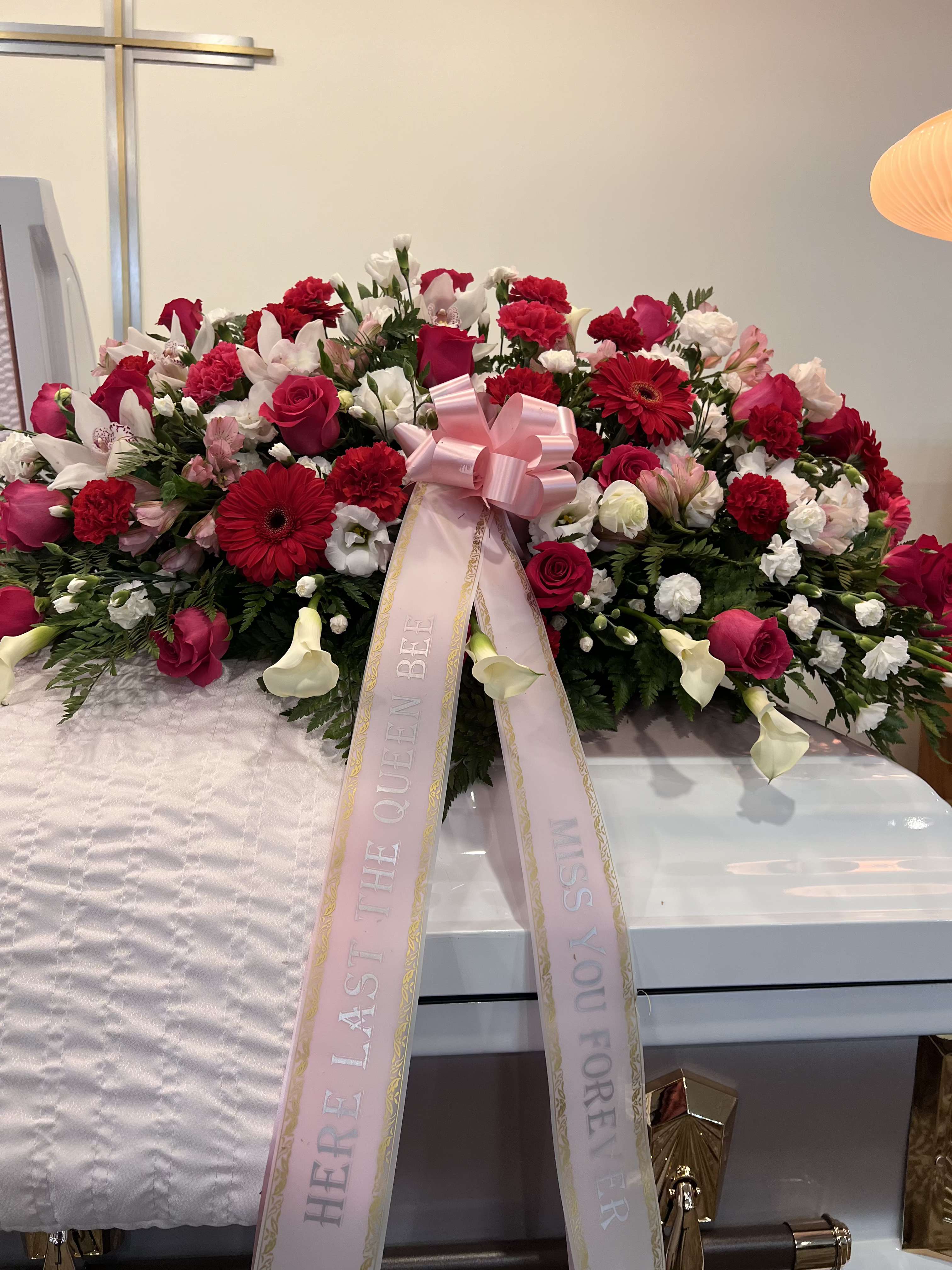 Large pink and red funeral spray with ribbon on a casket