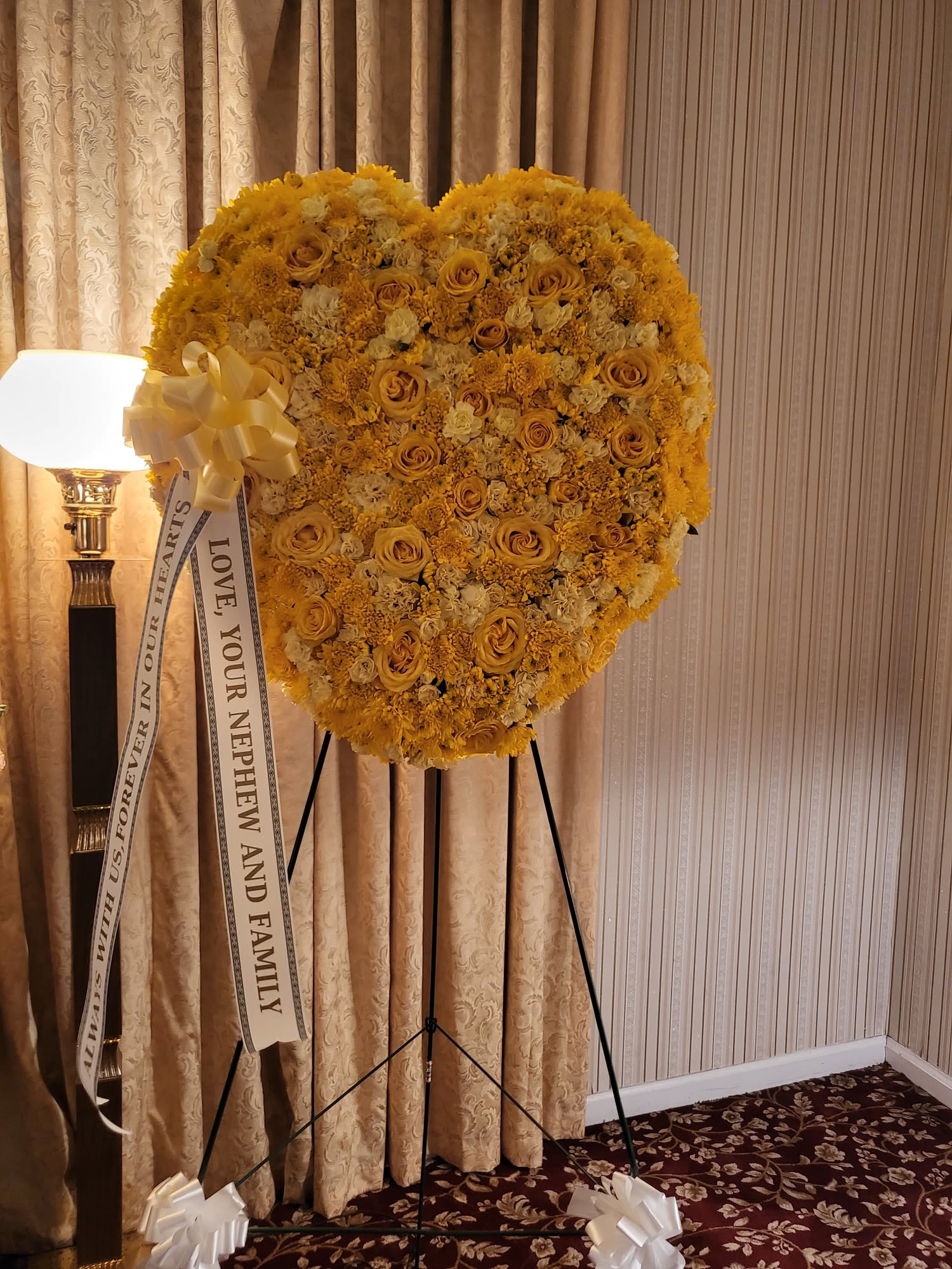 Heart-shaped yellow floral standing spray on an easel with a memorial ribbon