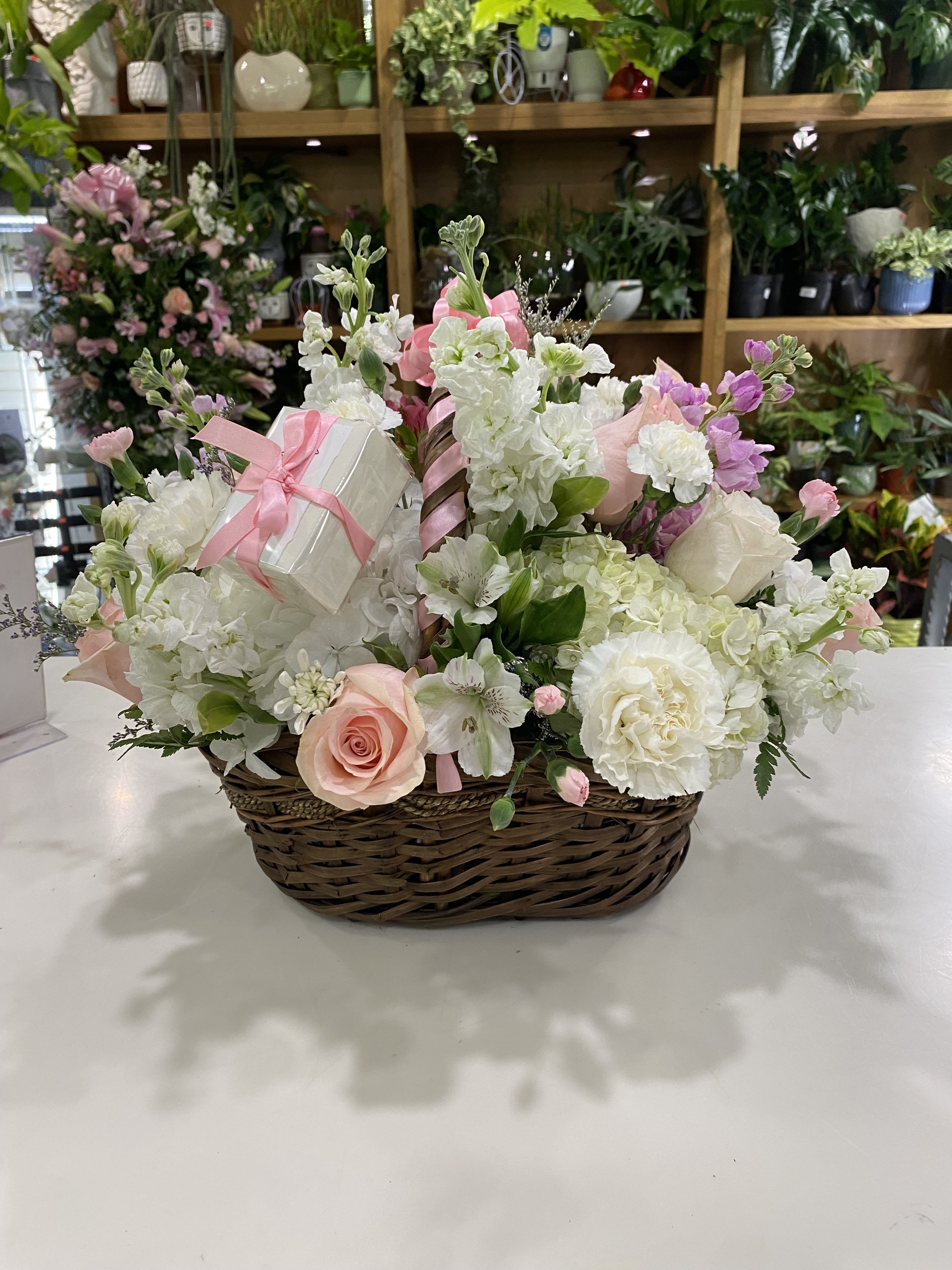 Basket arrangement of white and pink flowers with a small gift box and ribbon
