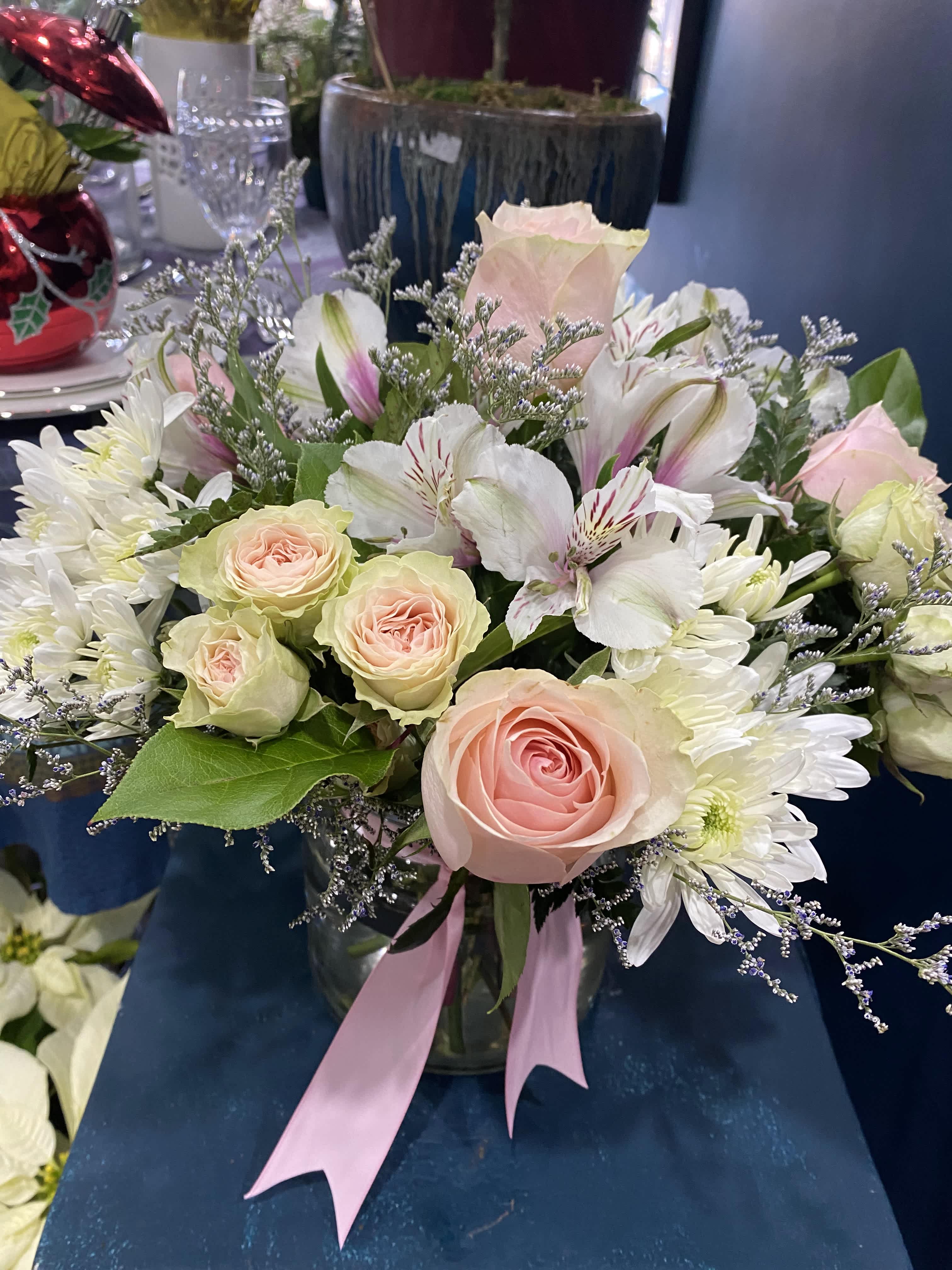 Pink roses and white flowers arranged in a glass vase with a pink ribbon