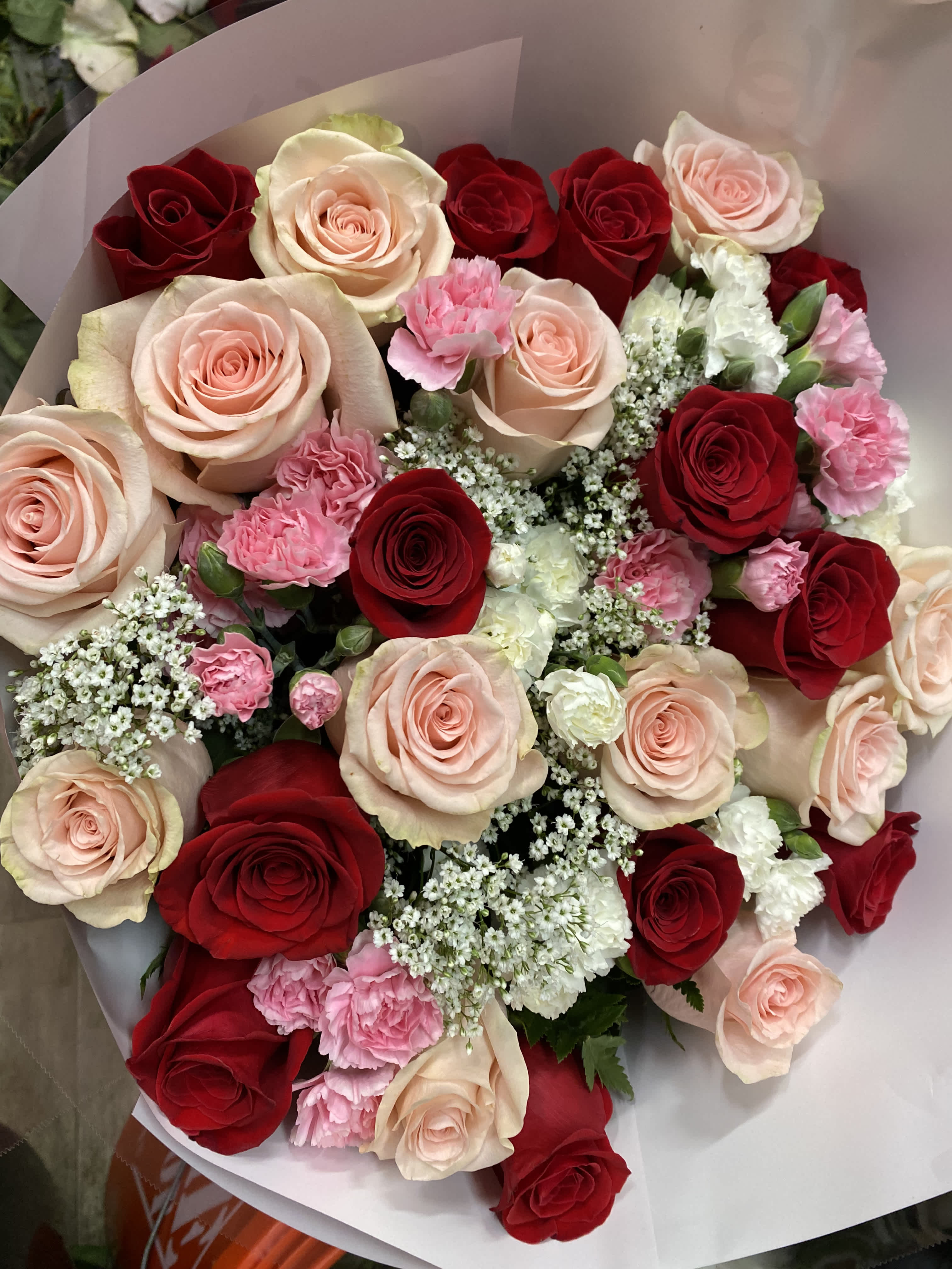 Bouquet of red and blush roses with pink carnations wrapped in pale paper