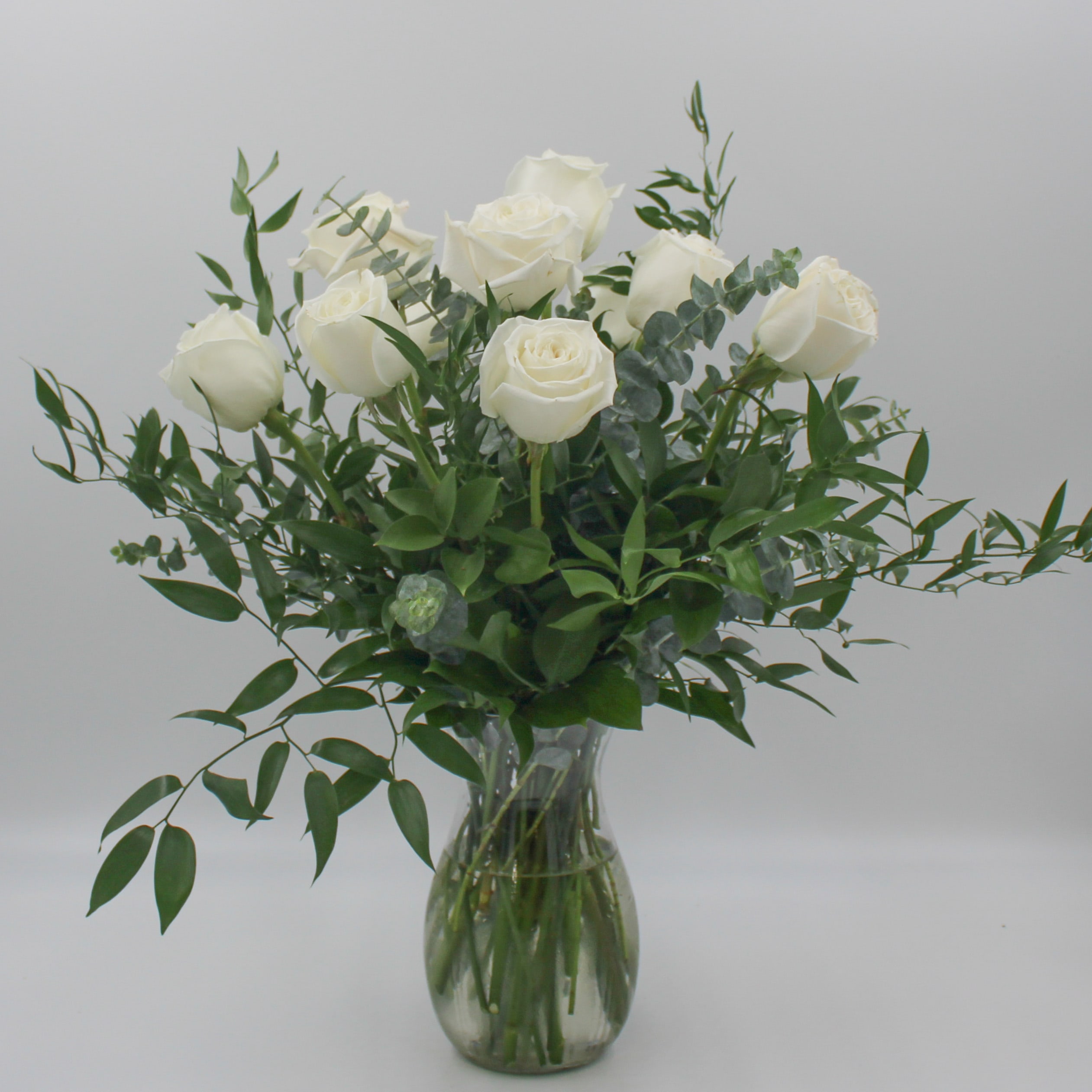 White roses in a clear glass vase with greenery