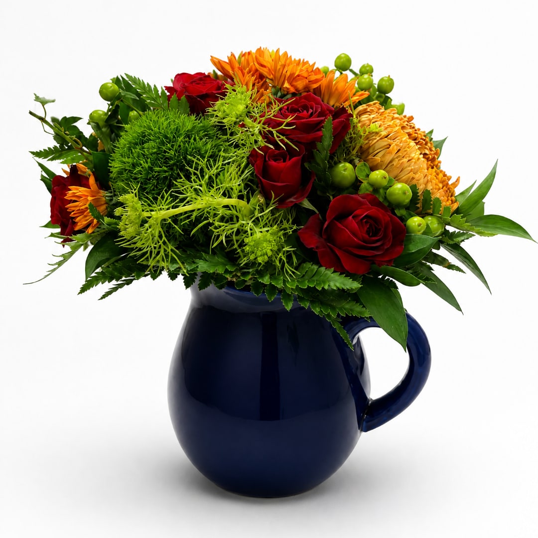 Red roses and orange flowers arranged in a dark blue pitcher vase