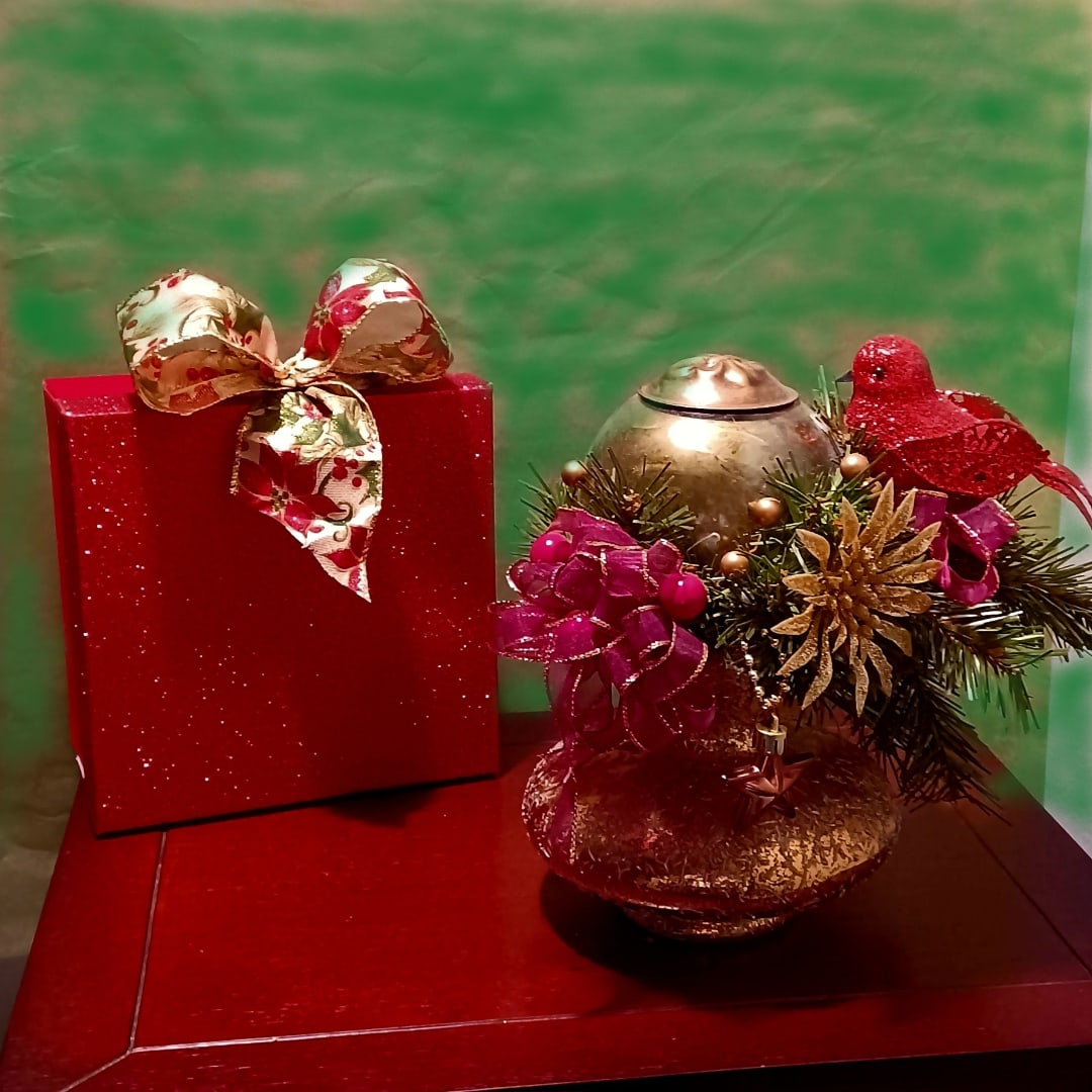 Red gift box with a decorative bow beside a gold holiday ornament arrangement