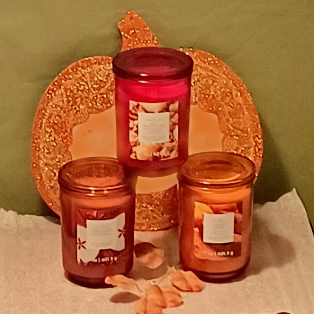 Three scented candles arranged in front of a glittery pumpkin decoration