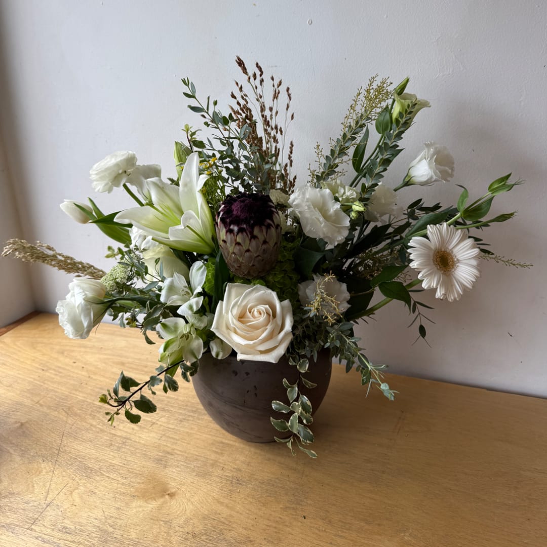 White floral arrangement in a dark vase with a central protea and rose