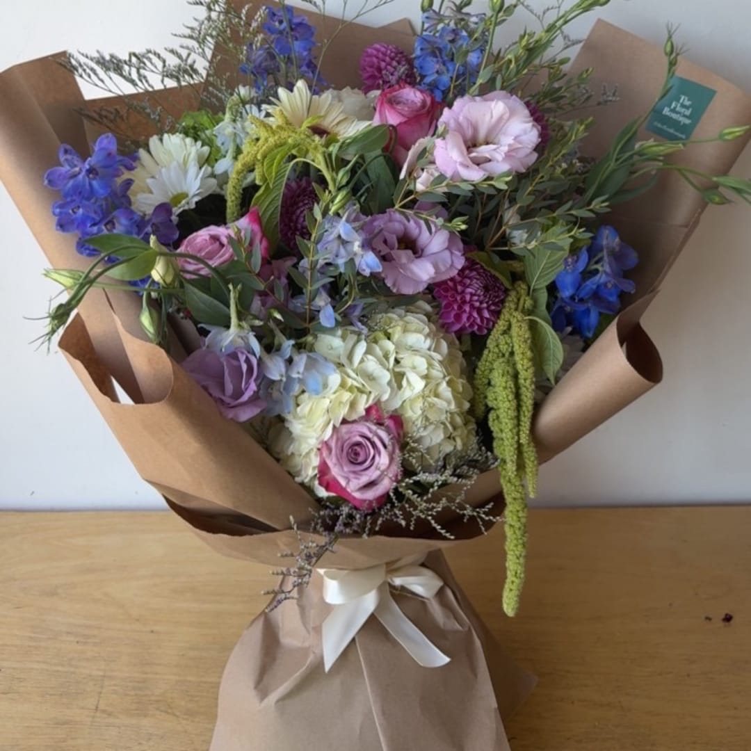 Mixed bouquet of pastel flowers wrapped in brown paper with a white ribbon