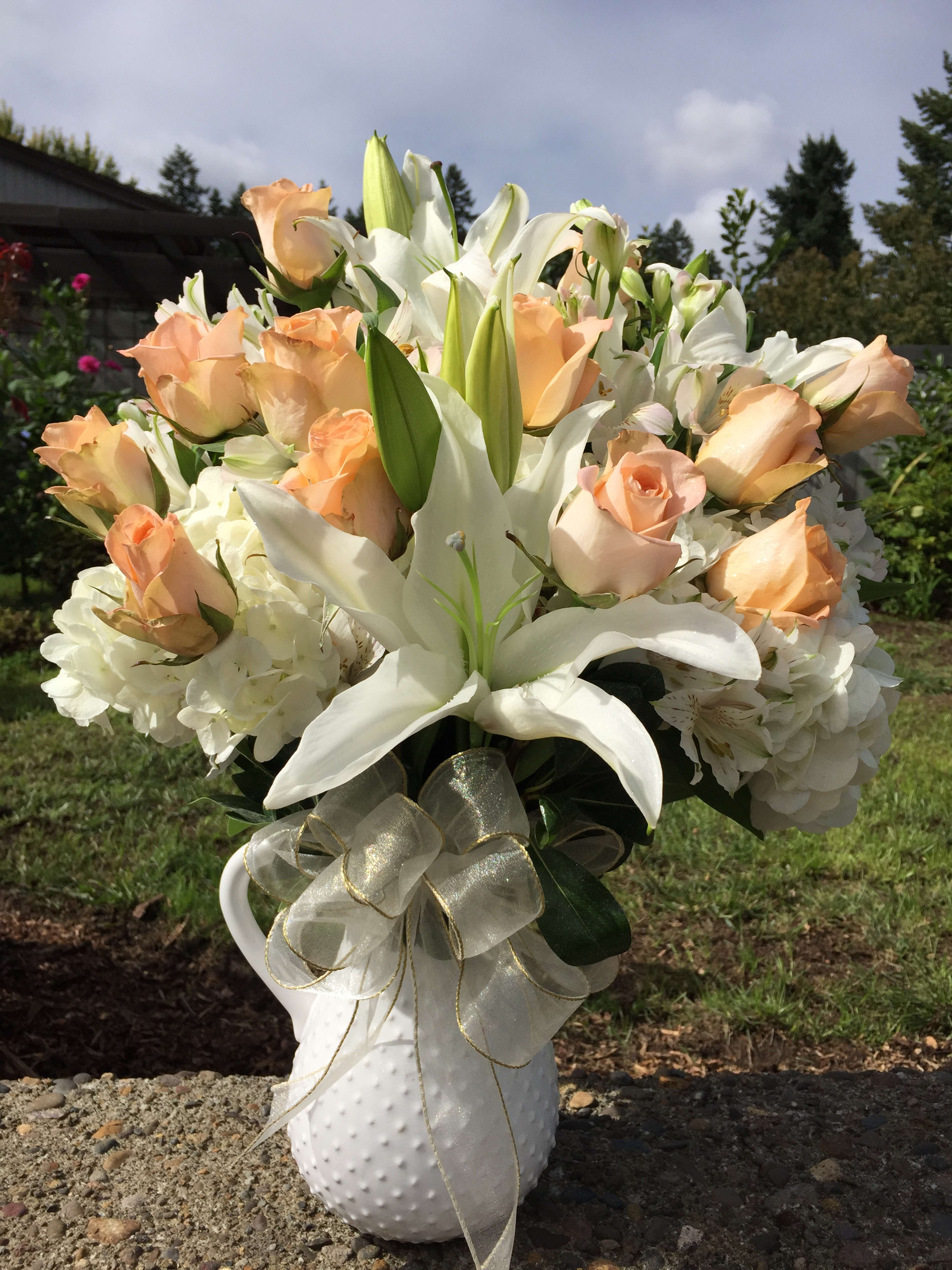 Peach roses and white lilies in a white vase with a ribbon bow