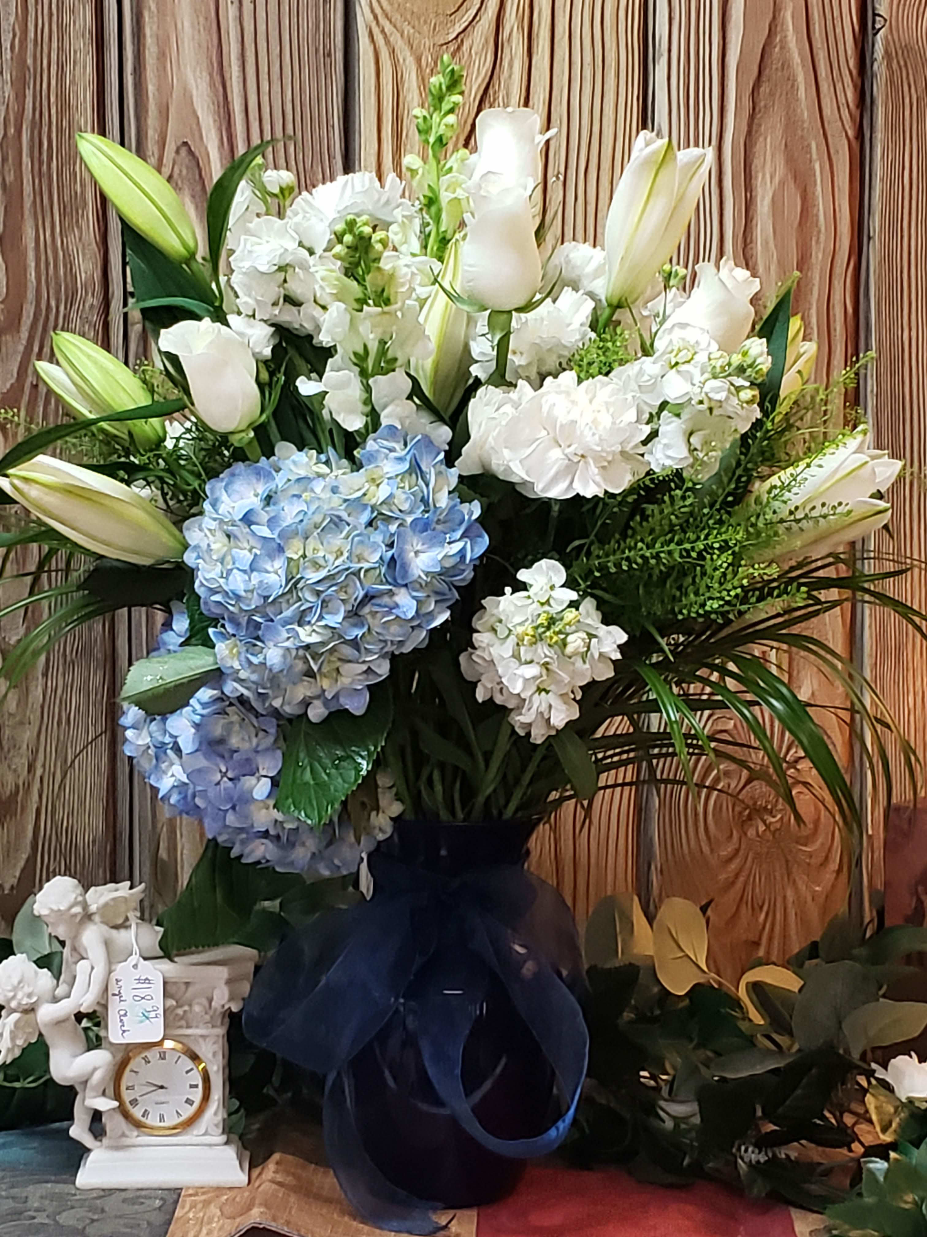 Large bouquet of white lilies, white blooms, and blue hydrangeas in a dark vase