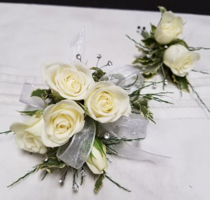 White rose corsages with silver ribbon and greenery